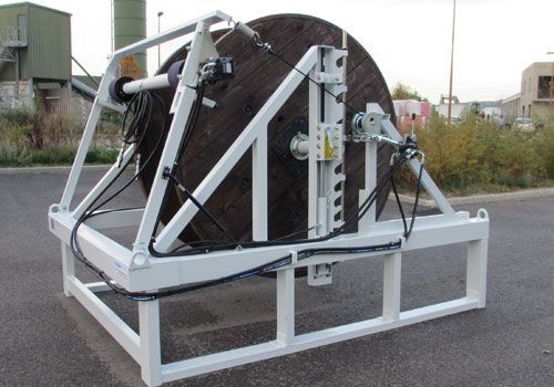 Support blanc pour enrouleur de câble contenant une grande bobine en bois, à l'extérieur.