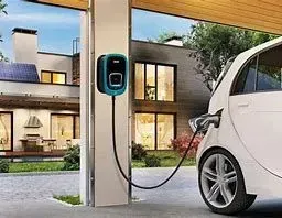 Un coche eléctrico se está cargando en una estación de carga frente a una casa.