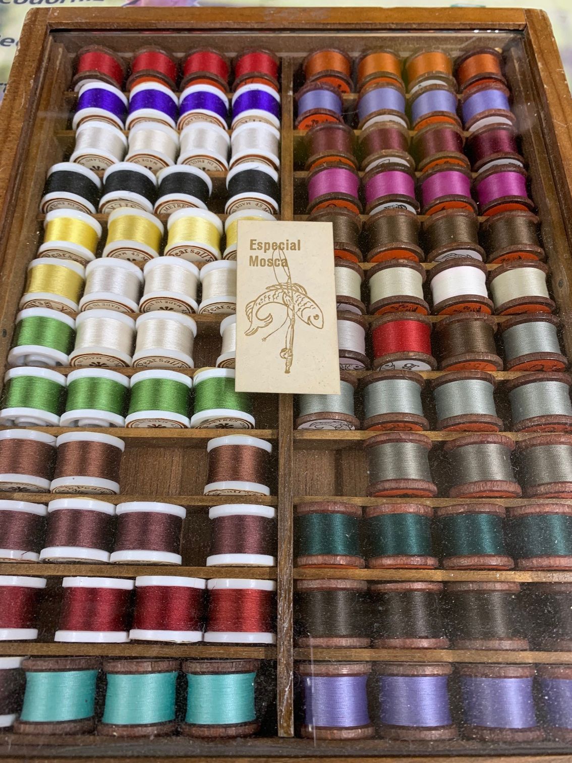 Una caja de madera llena de carretes de hilo de diferentes colores.