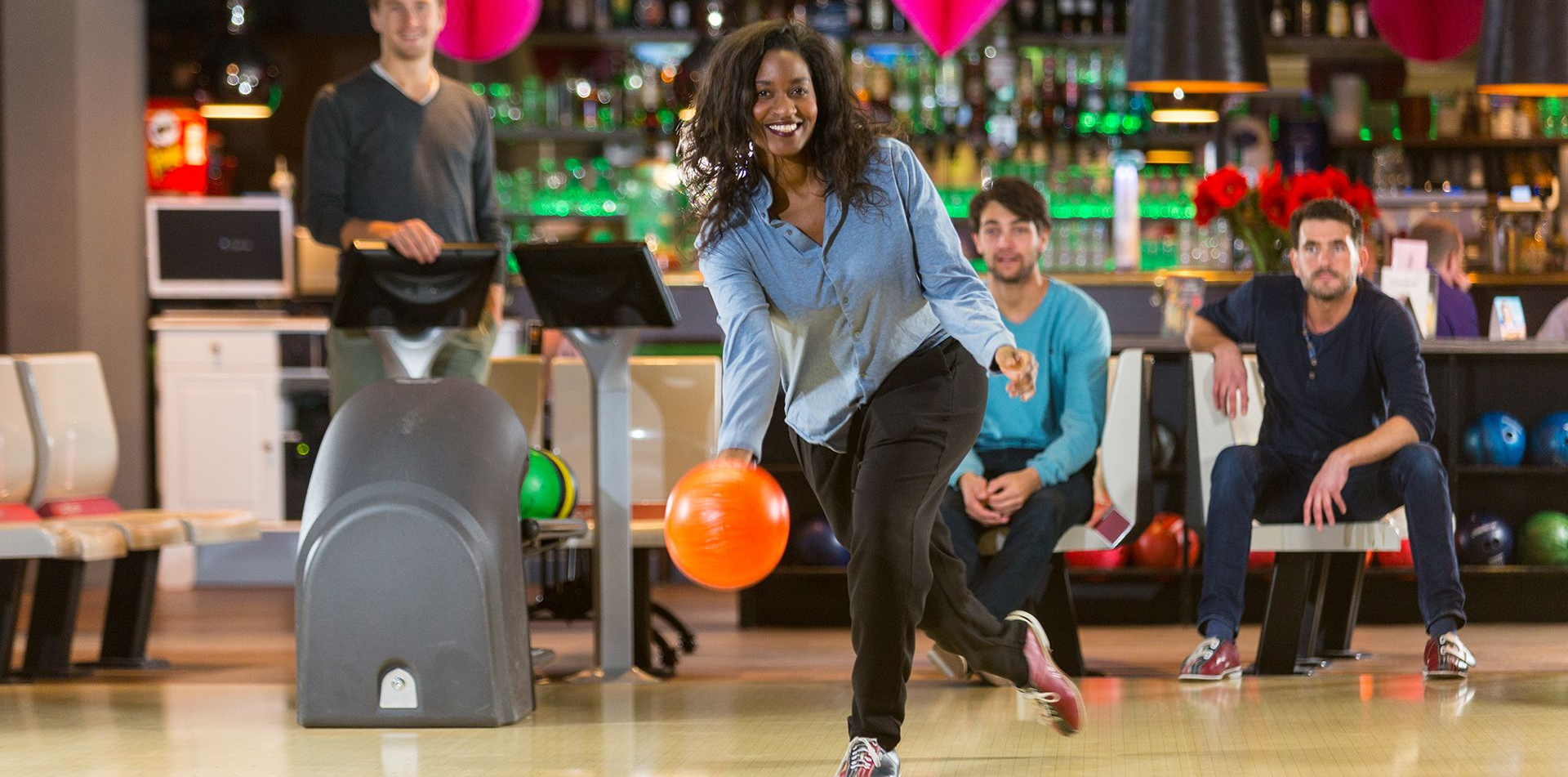 Vrouw die met vrienden bowlt in een bowlingbaan en een bal gooit.