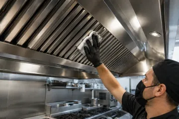 Un chef limpia con un paño la campana extractora de acero inoxidable de una cocina profesional.