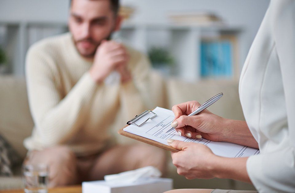 Person schreibt etwas auf ein Formular, gegenüber sitzt ein Mann