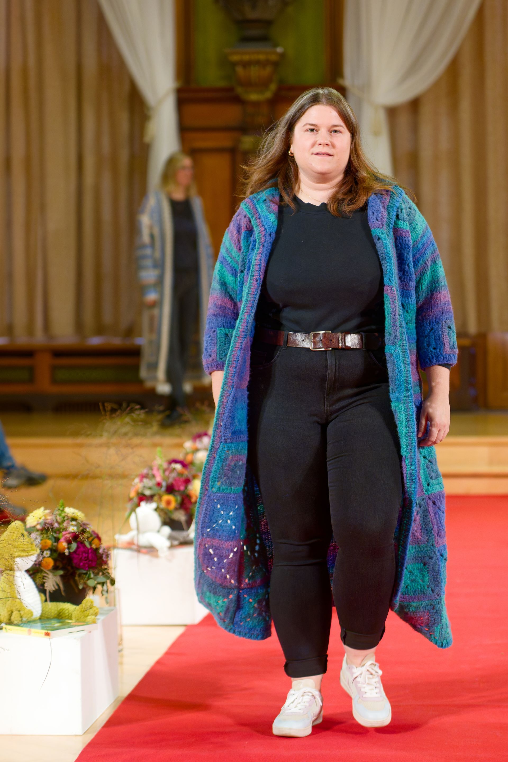 Frau in blauem Strickmantel schreitet über den roten Teppich.