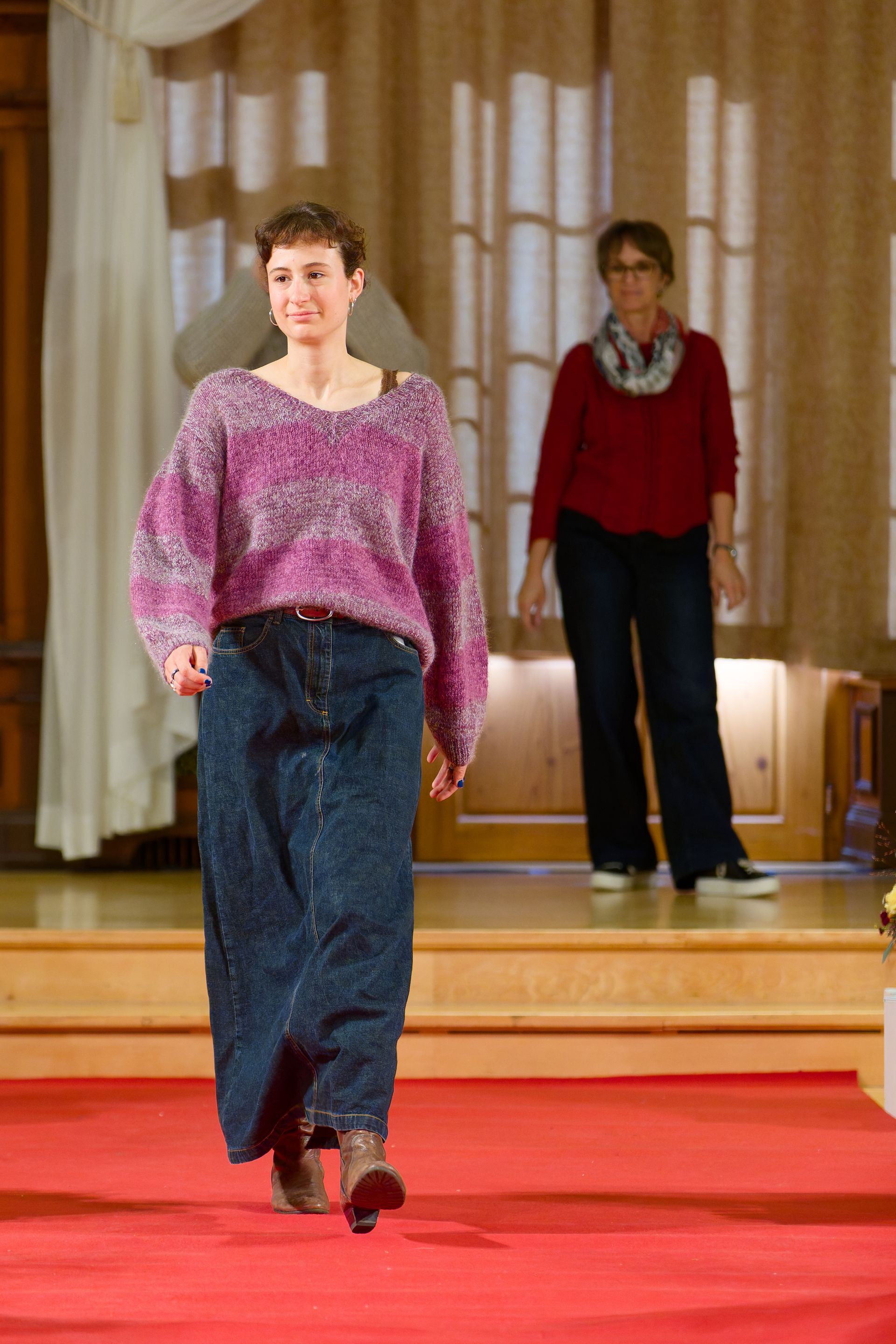Person in einem lila Pullover & einem Jeansrock schreitet über einen roten Teppich.