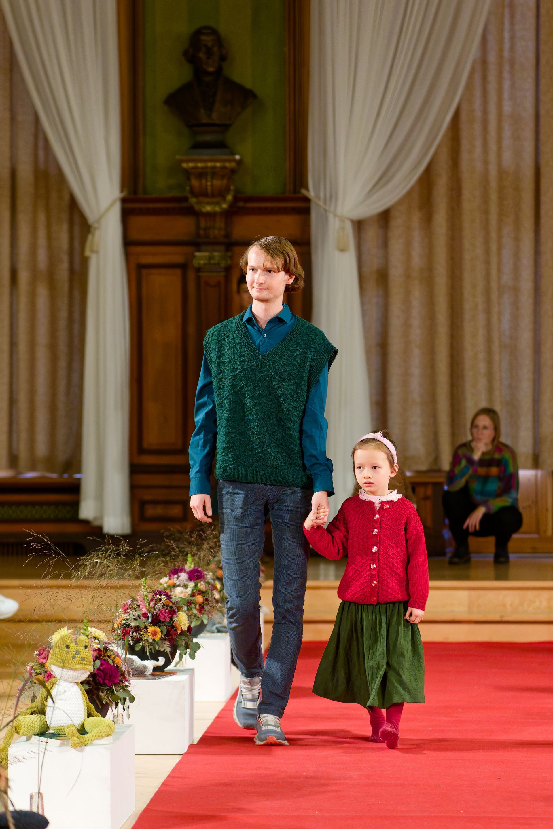 Ein Junge in grüner Weste und ein Mädchen in rotem Mantel laufen Händchen haltend über den Laufsteg.