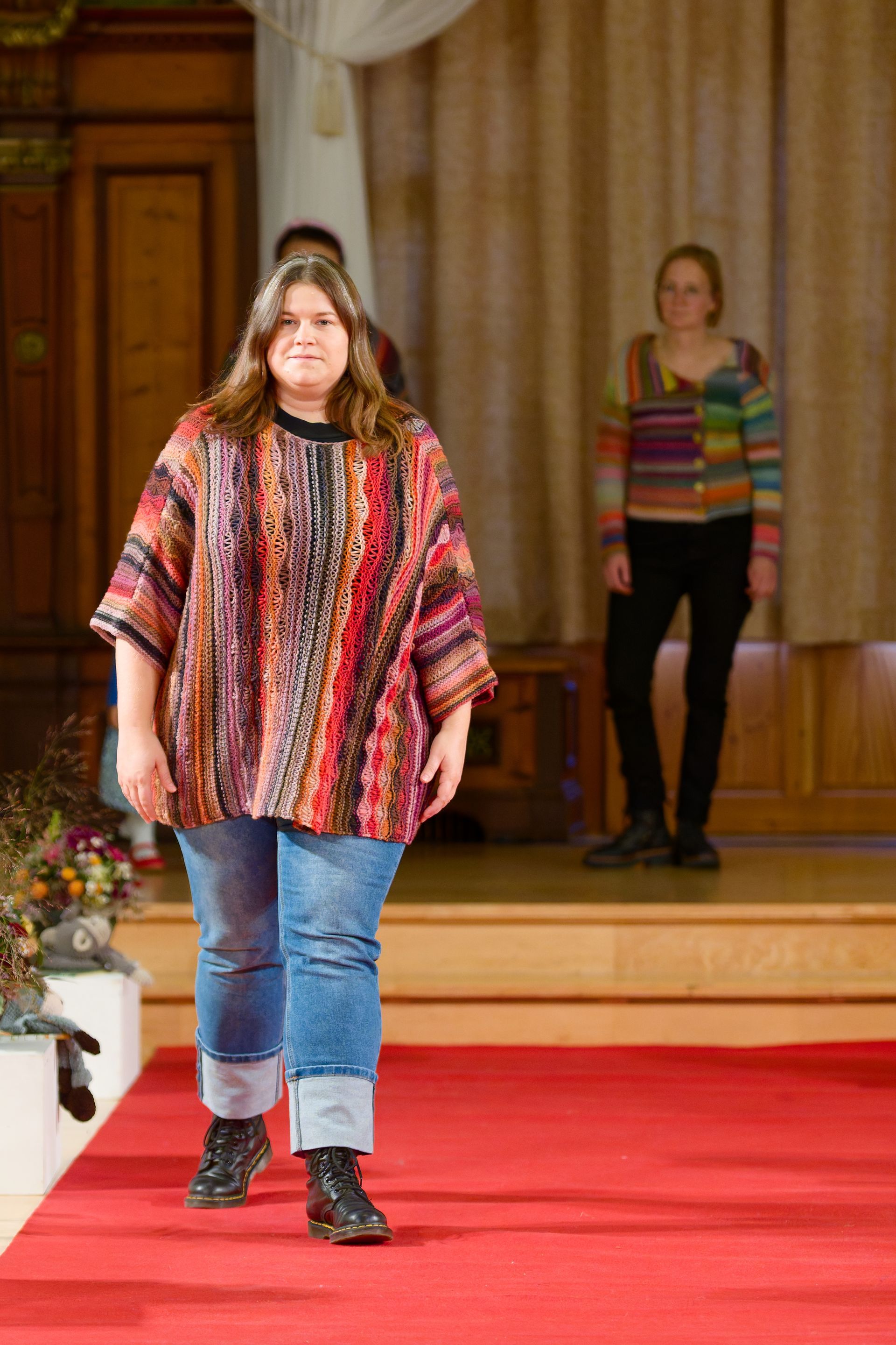 Eine Frau in einem farbenfrohen Stricktop und Jeans schreitet über den roten Teppich.