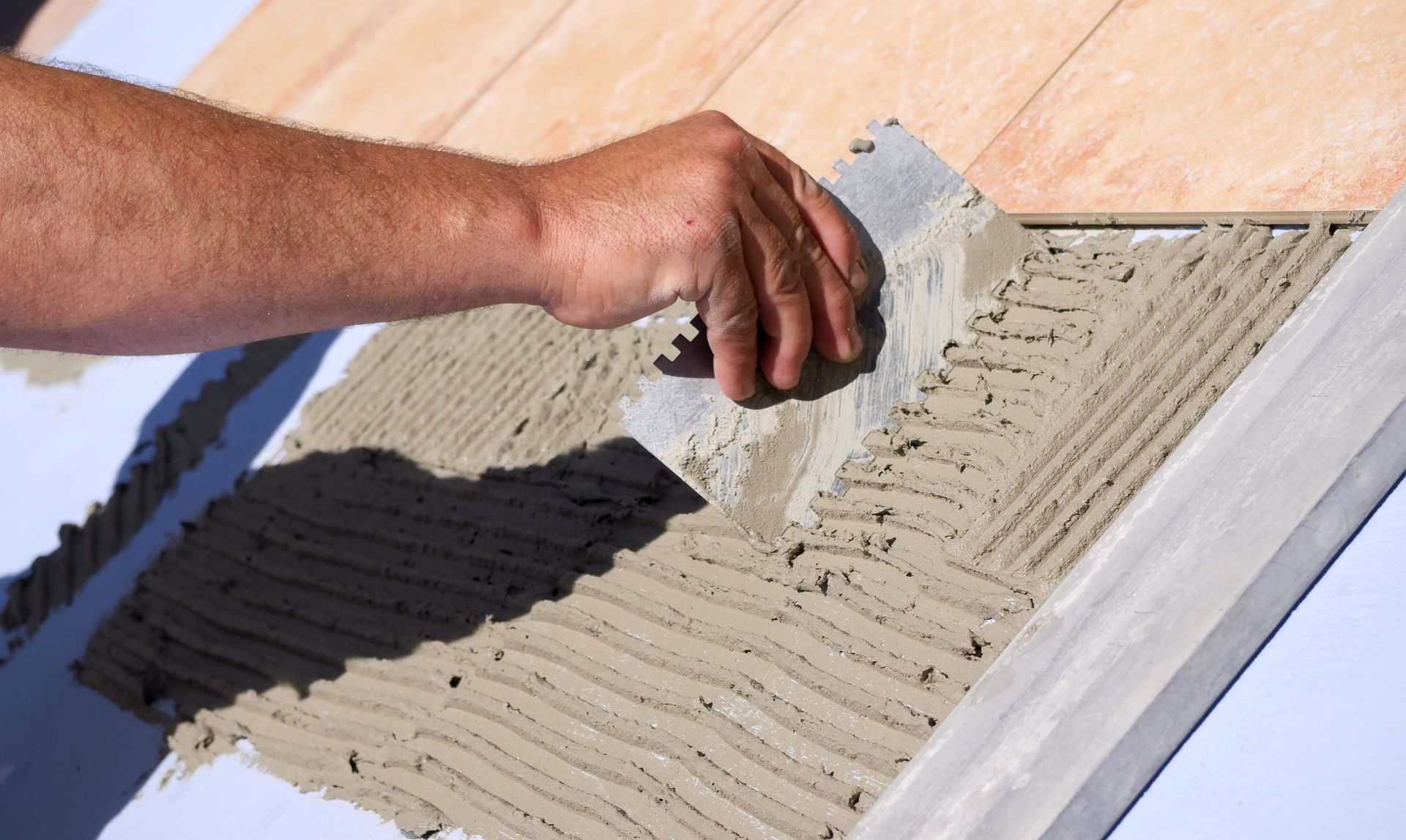 Mur de salle de bains dont des carreaux manquants laissent apparaître le mur brun en dessous. Les murs environnants sont carrelés en blanc.