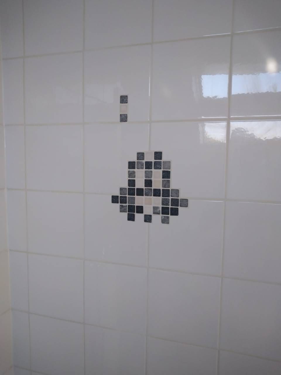 Mosaïque Space Invader sur un mur carrelé blanc dans une salle de bains.
