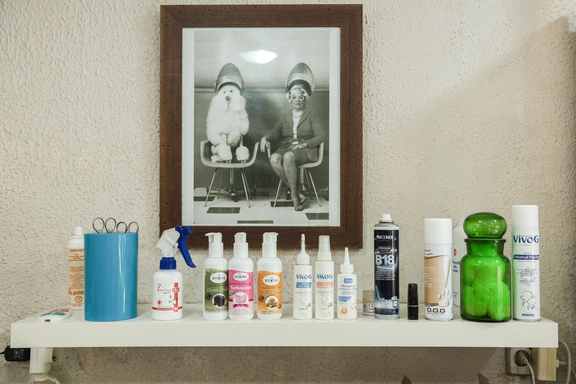 Étagère de salle de bains avec des articles de toilette assortis sous une photo encadrée en noir et blanc, sur un mur beige.
