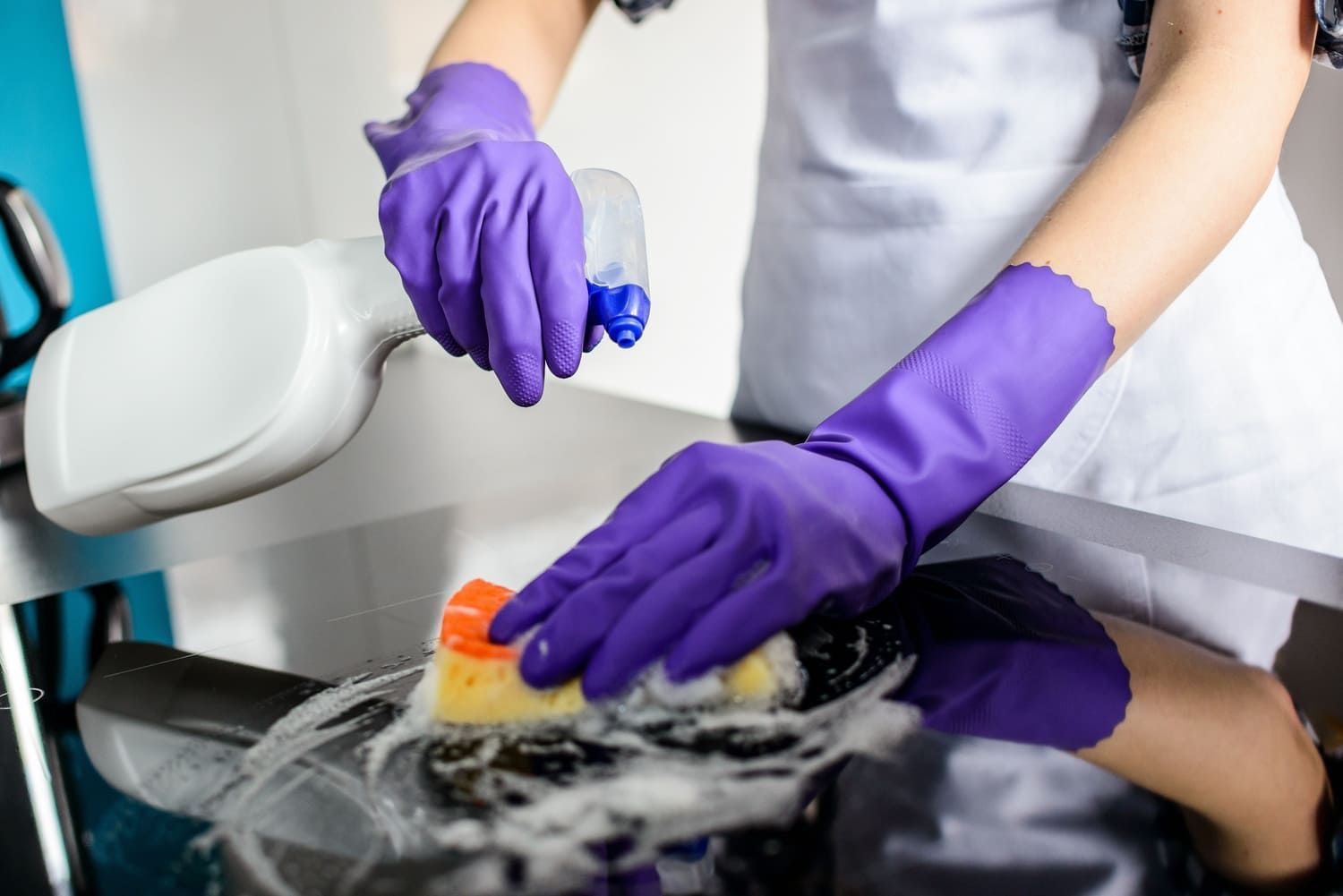 Una mujer que lleva guantes morados está limpiando una silla con una esponja y spray.