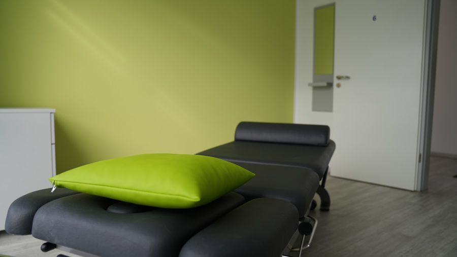 Eine Massageliege mit einem grünen Kissen darauf in einem Zimmer.4