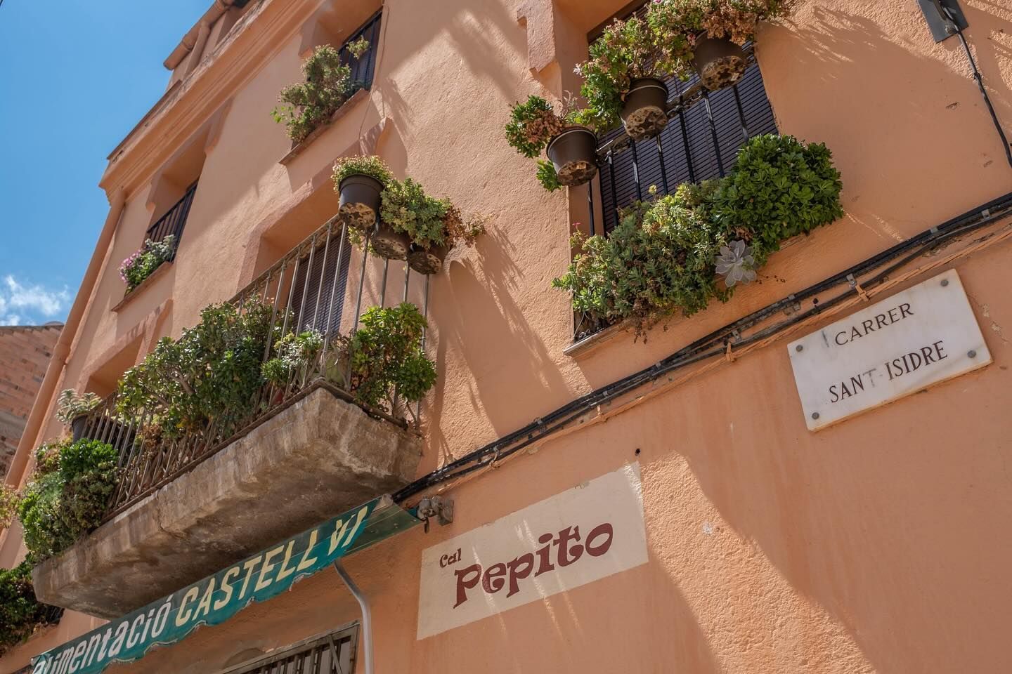 Dos mujeres en una cocina: una sentada haciendo el signo de la paz, la otra preparando comida junto a la estufa.