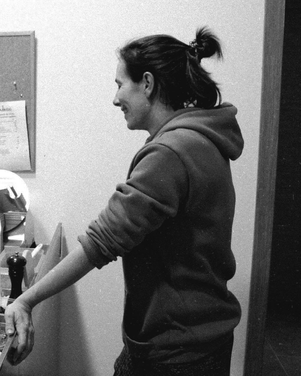 Mujer con sudadera con capucha sonríe, mirando hacia la izquierda, con un pequeño moño. Apoyada en el mostrador.