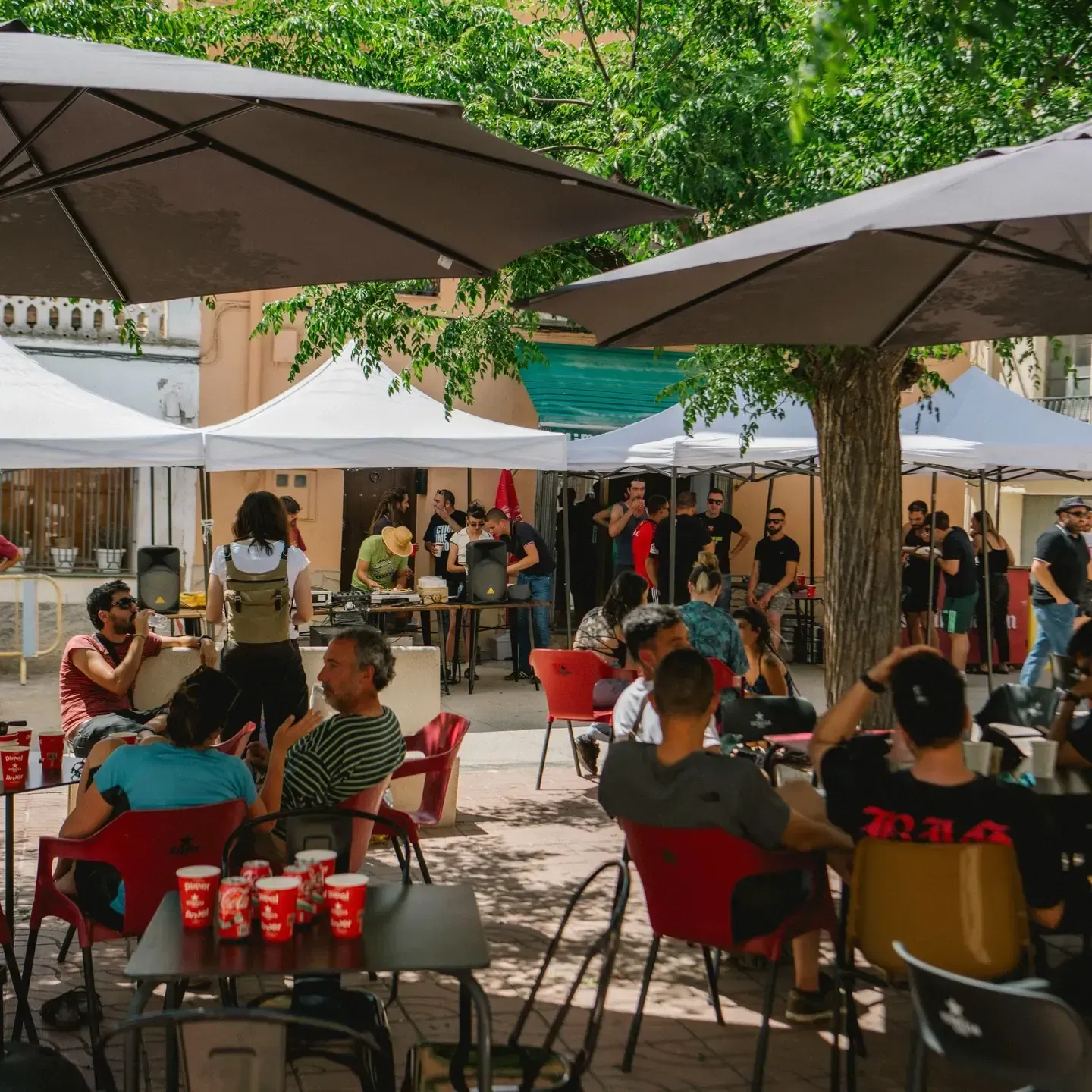 Mercado al aire libre con sombrillas, gente paseando y vendedores.