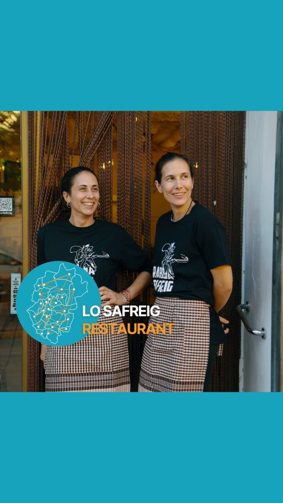 Dos mujeres sonrientes, vestidas con delantales y camisetas a juego con el logo de un restaurante, posan frente a él. Fondo turquesa.