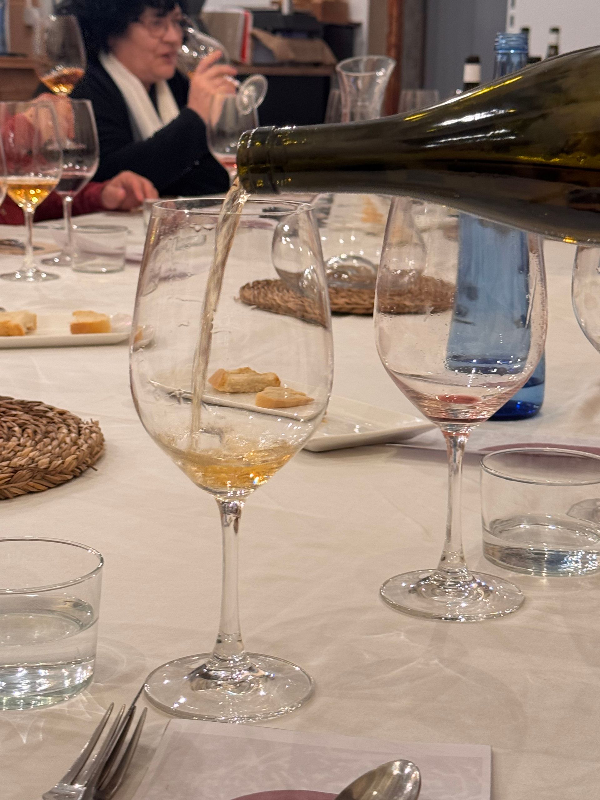 Vi que s'aboca en una copa en un tast, altres copes i gent al fons.