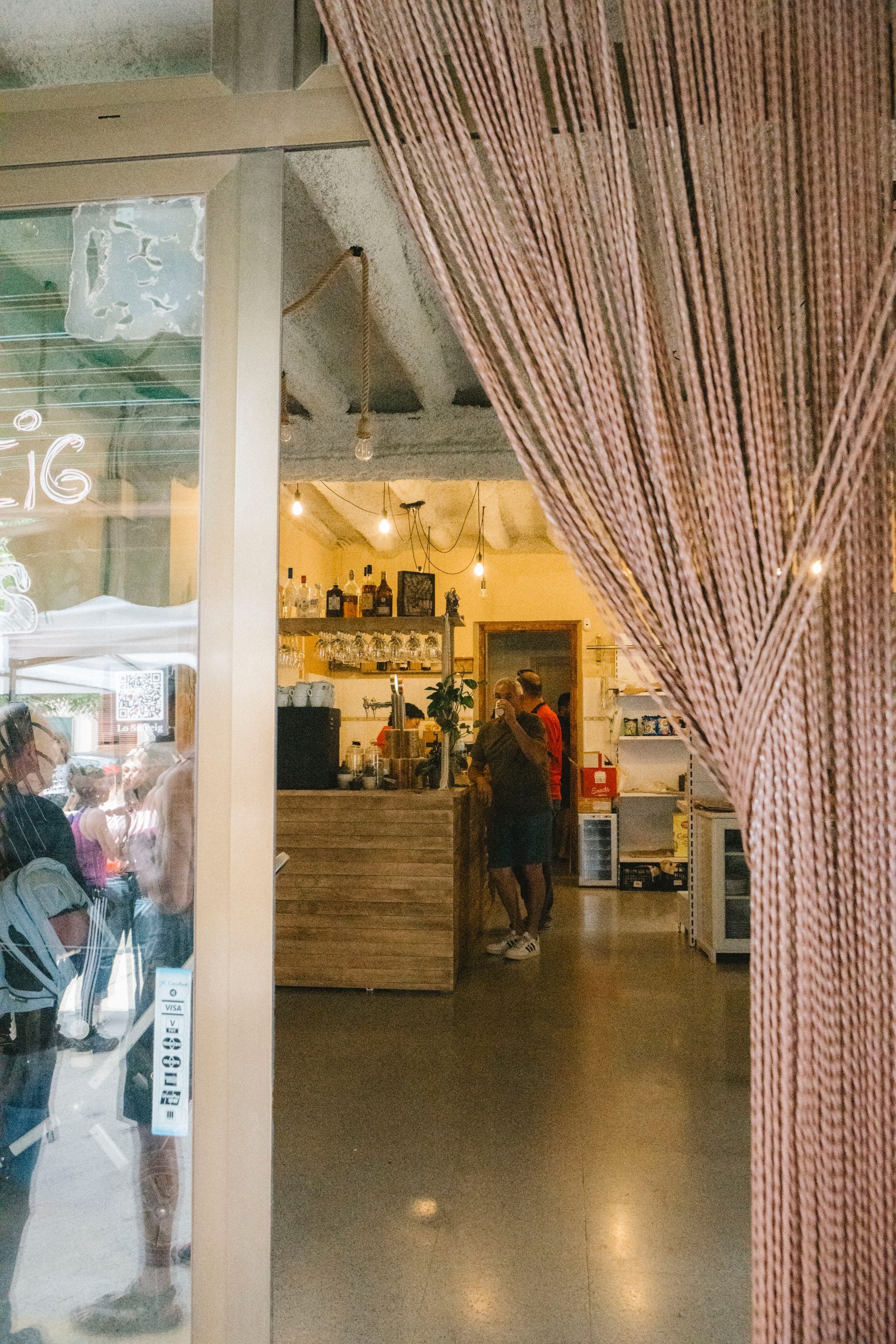 Interior de botiga amb cortina de perles. Gent en un taulell, façana de la botiga visible.