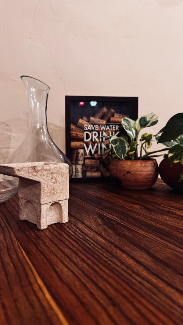 Mano sosteniendo una tarjeta color verde azulado con texto dorado dentro de un restaurante, fondo desenfocado con mesas y sillas.