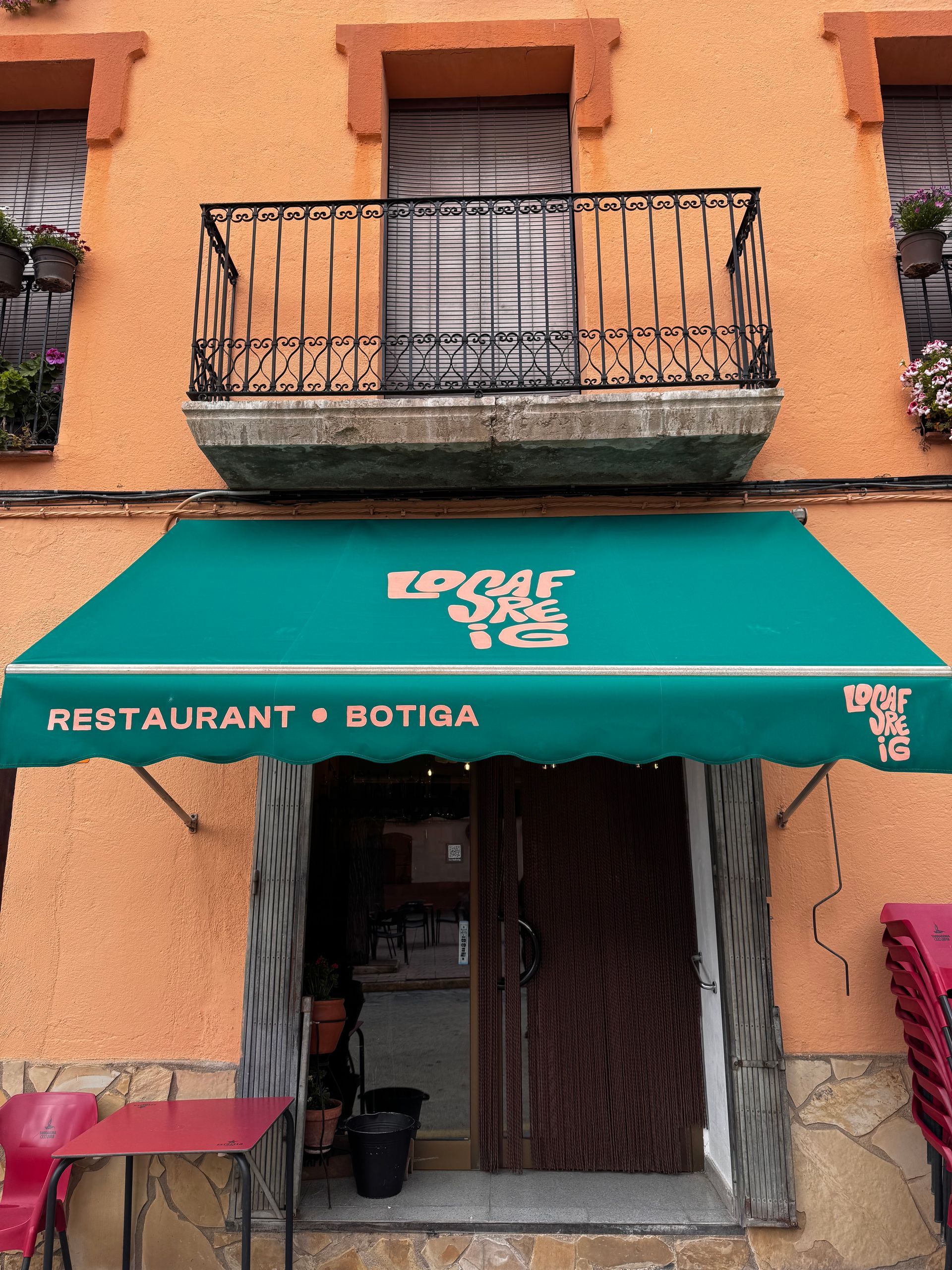 Entrada de restaurant amb tendal verd i balcó negre en un edifici taronja. A sota hi ha escrit 