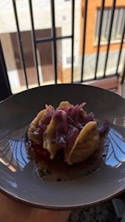 Un plat de menjar amb boletes daurades, cebes vermelles i tomàquets, a prop d'una finestra.