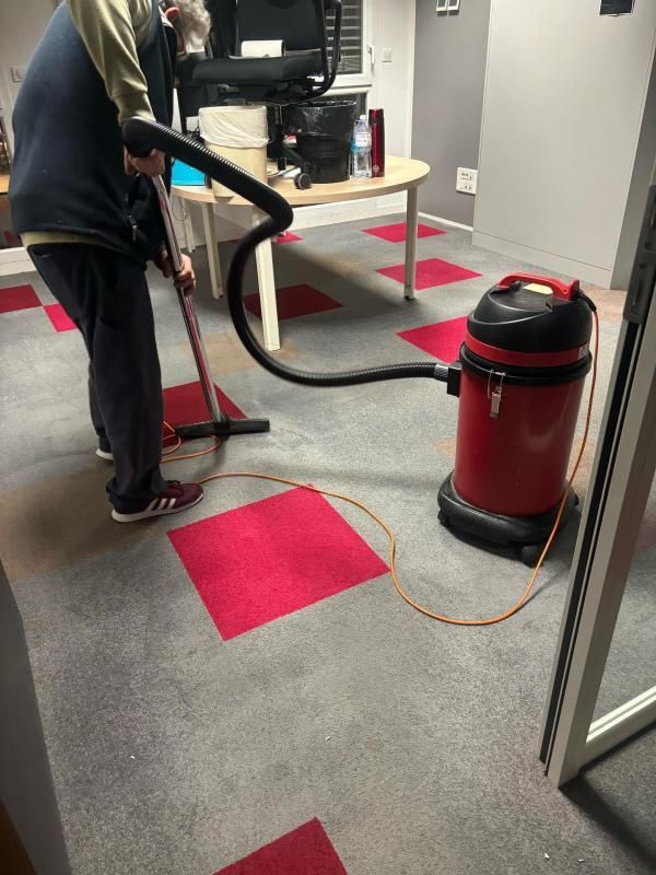 Une personne passe l'aspirateur sur une moquette aux carrés de couleur grise et rose