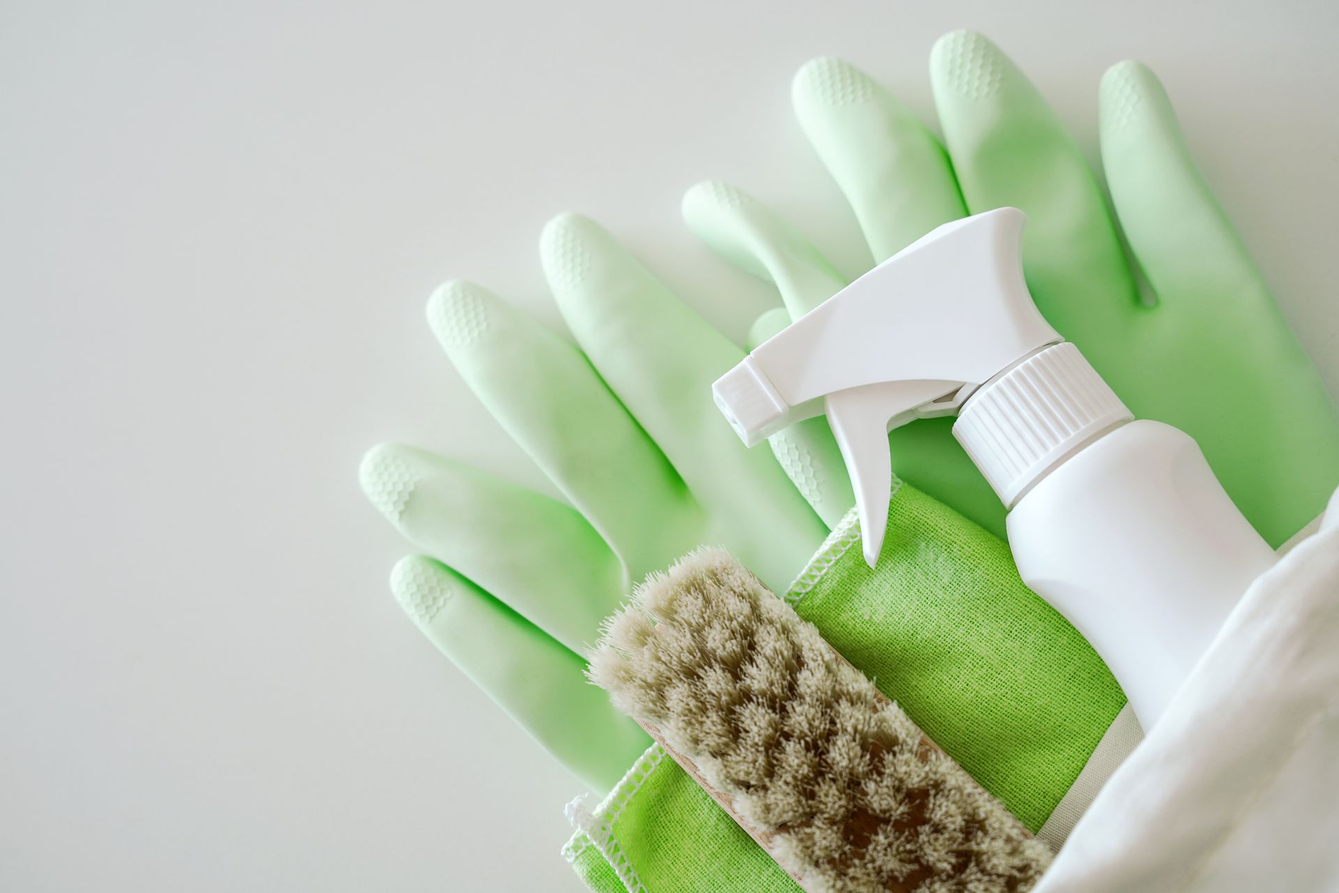 Produit ménager et brosse posés sur des gants en latex vert