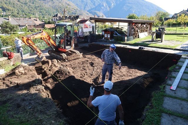 Operai che scavano un cortile per realizzare una piscina, utilizzando un escavatore e strumenti di misurazione.