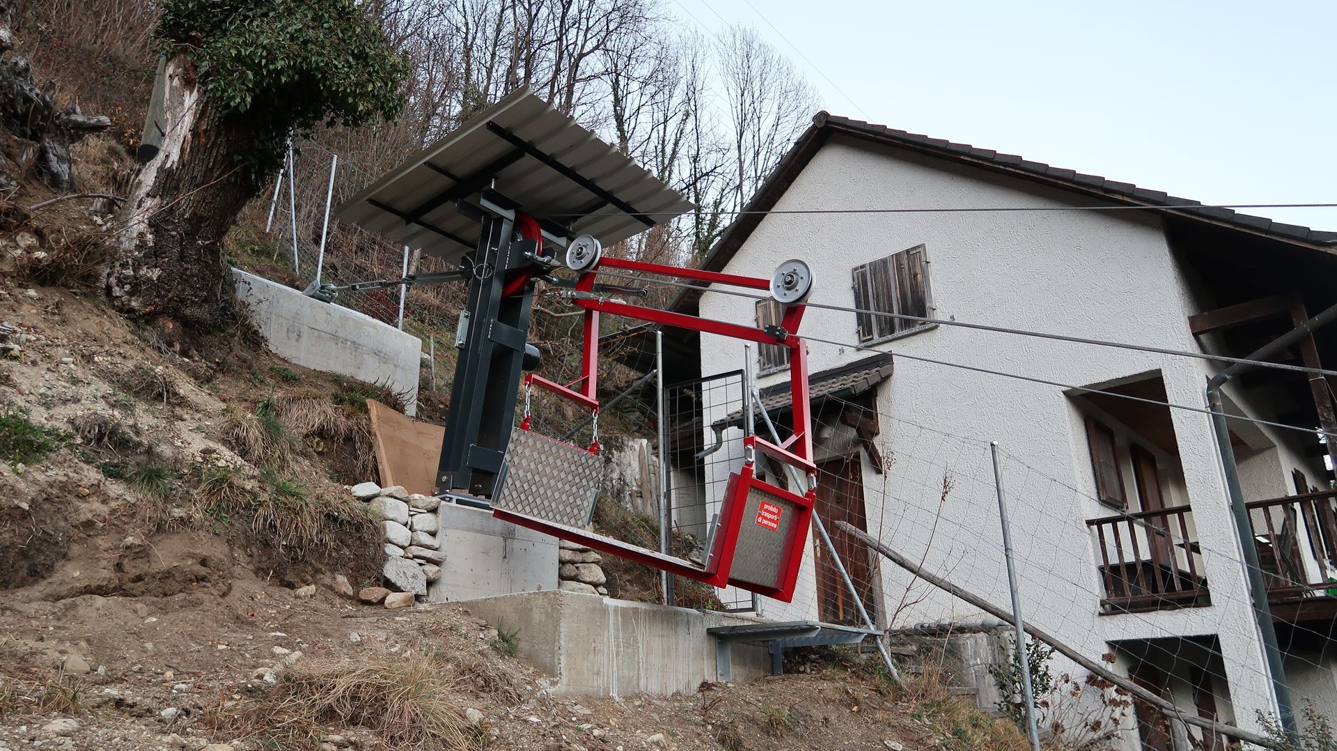 Una seggiovia rossa e nera su una collina accanto a una casa bianca con le persiane marroni.