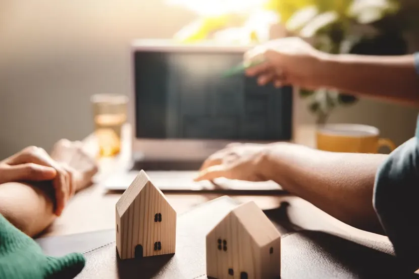 Person, die drinnen an einem weißen Tisch an einem Laptop arbeitet und auf der Tastatur tippt.