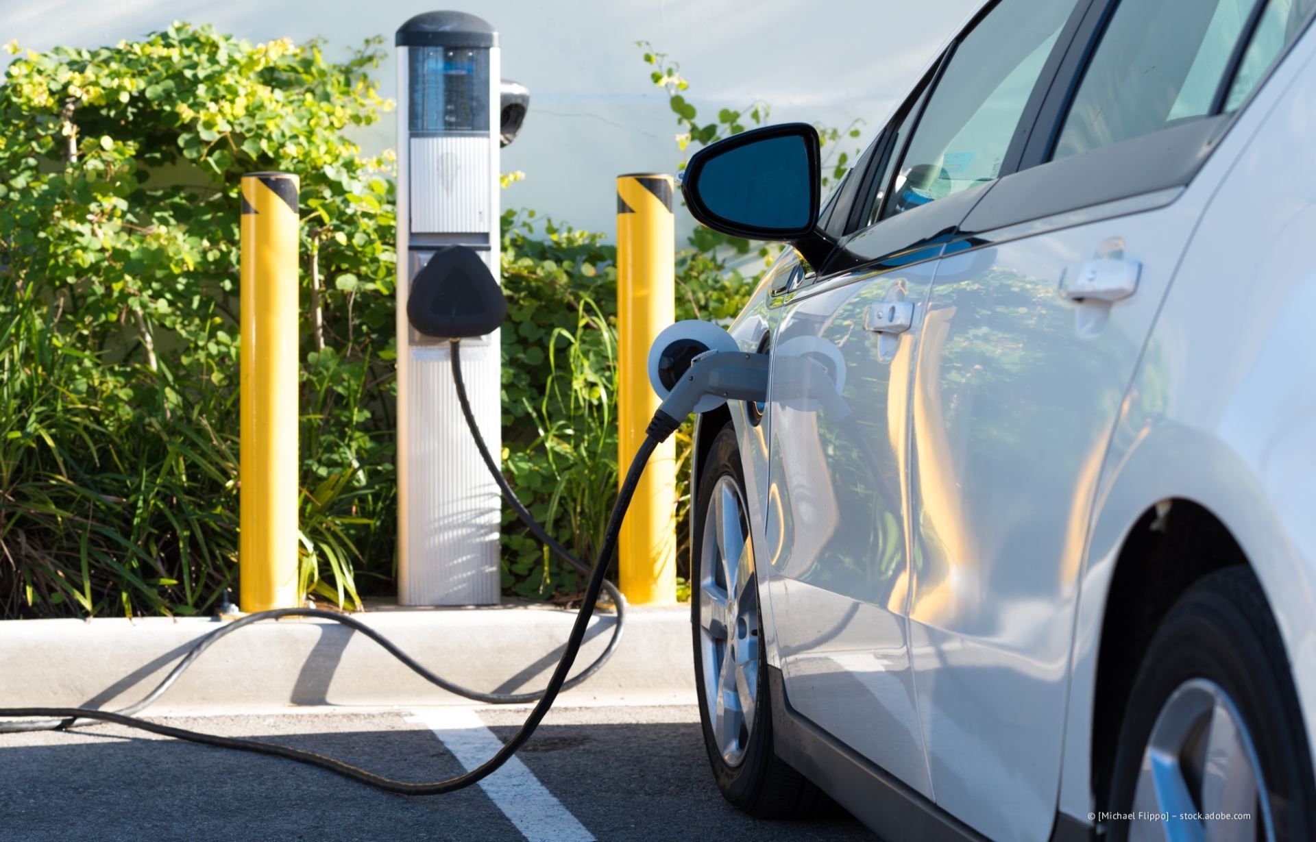 Weißes Elektroauto lädt bei Tageslicht an einer öffentlichen Ladestation im Freien.