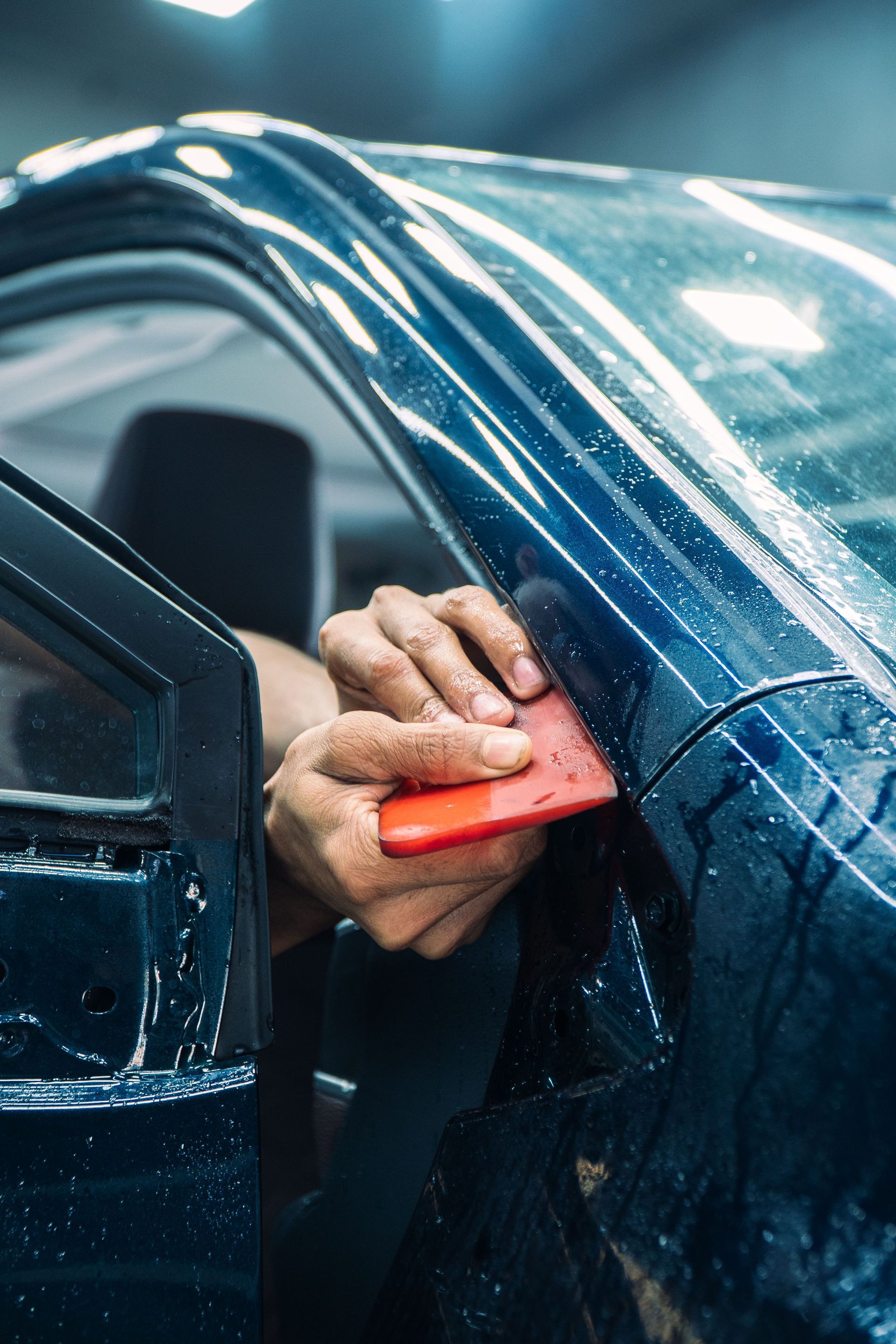 Persona limpiando la ventana de un coche con un paño y una escobilla limpiacristales