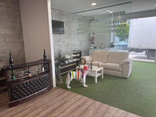 Una fotografía interior muestra una oficina con un bar, un sofá blanco y una estatua de bulldog pintada. Hay un camión estacionado afuera.
