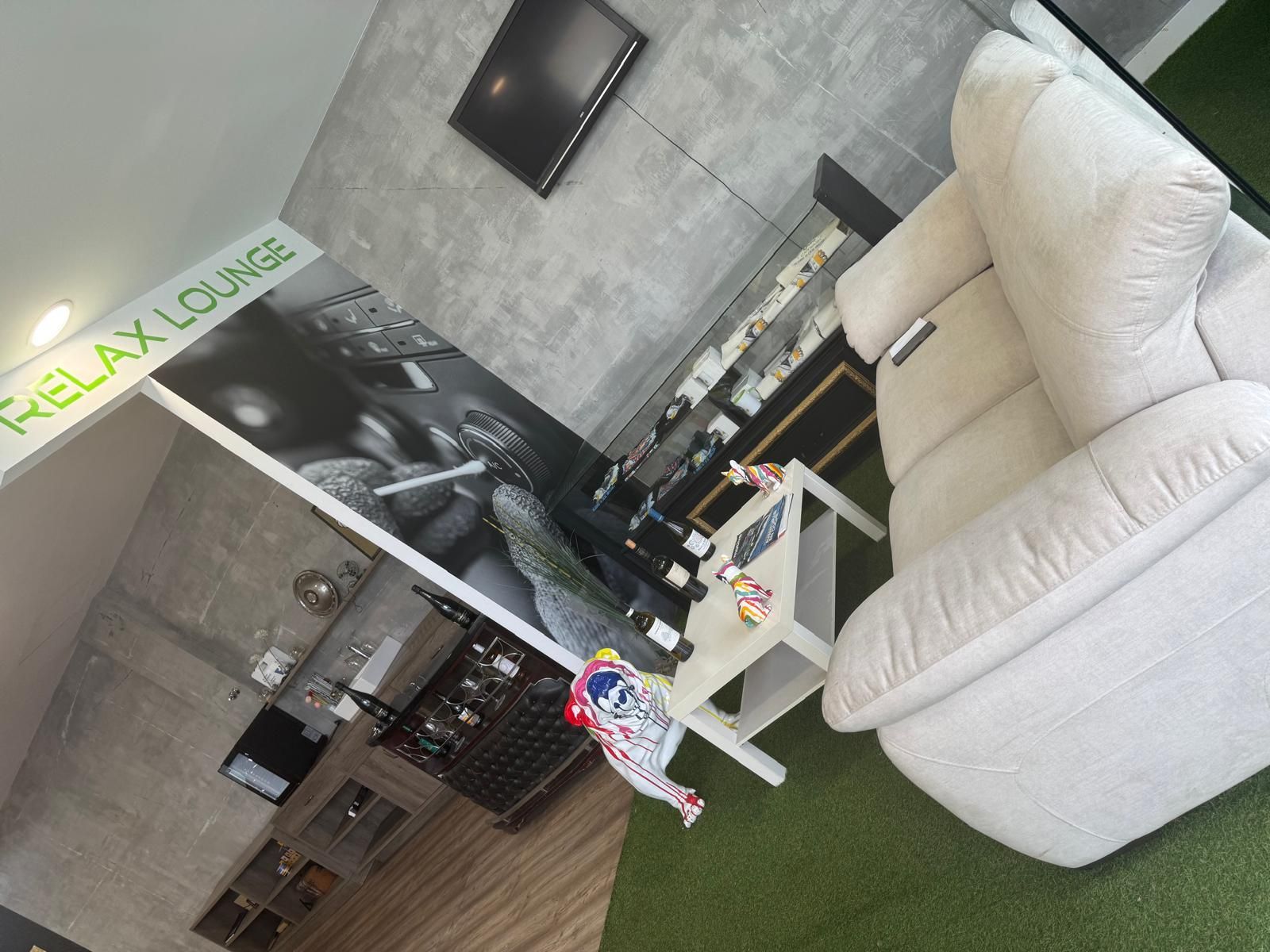 Un área “Relax Lounge” con un sillón reclinable blanco, una mesa pequeña y una pared decorativa con un gráfico en blanco y negro.