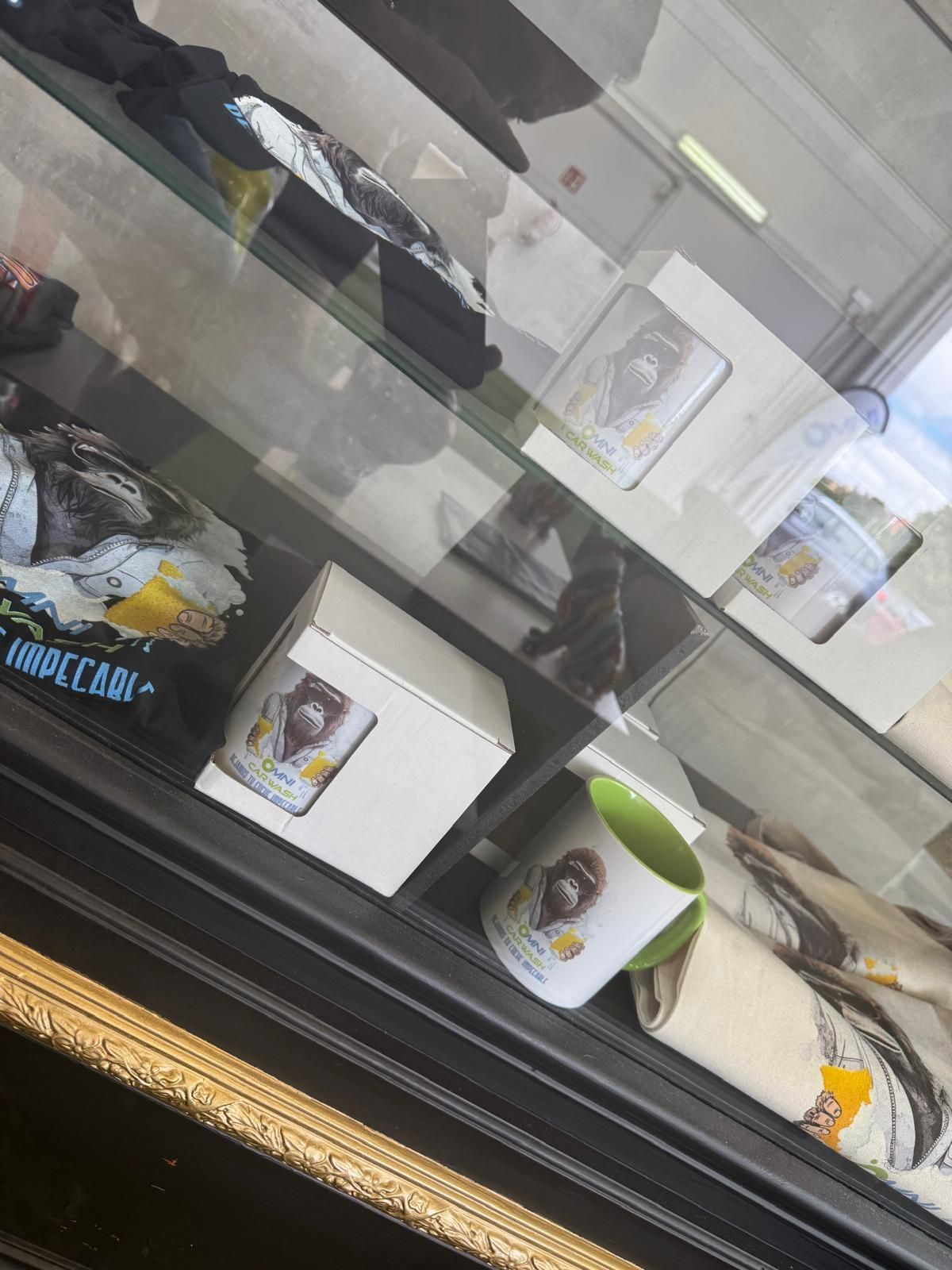 Vitrina con mercancía, incluyendo tazas y una camiseta. Algunos artículos tienen detalles en amarillo y verde.