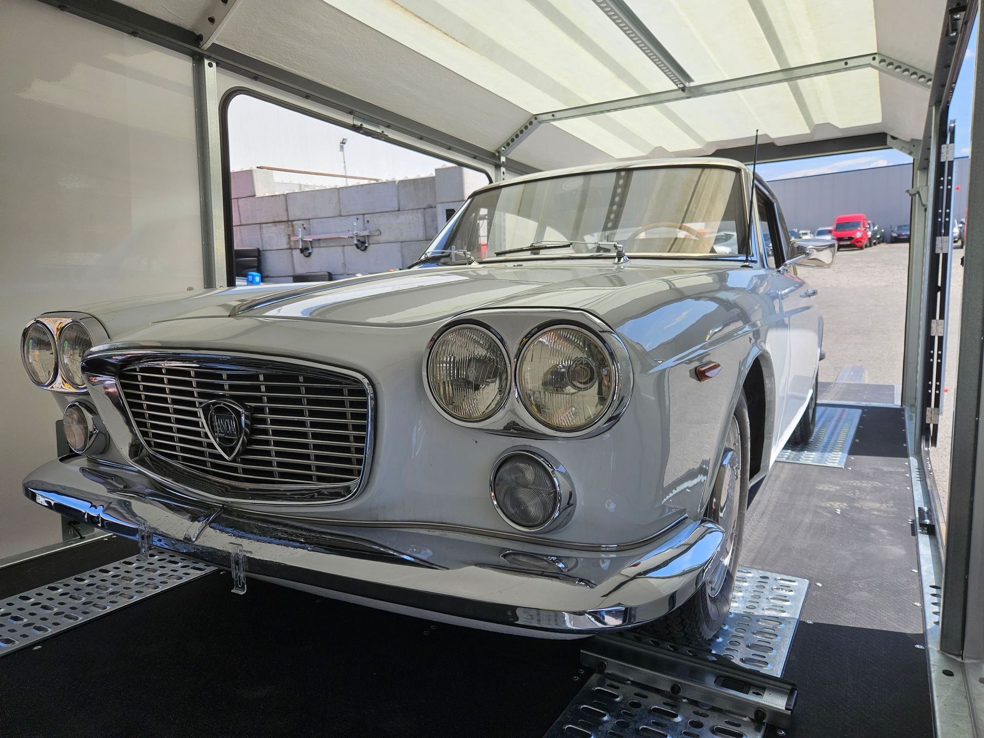 Une Lancia Flavia coupée blanche d'époque est garée à l'intérieur d'une remorque fermée.