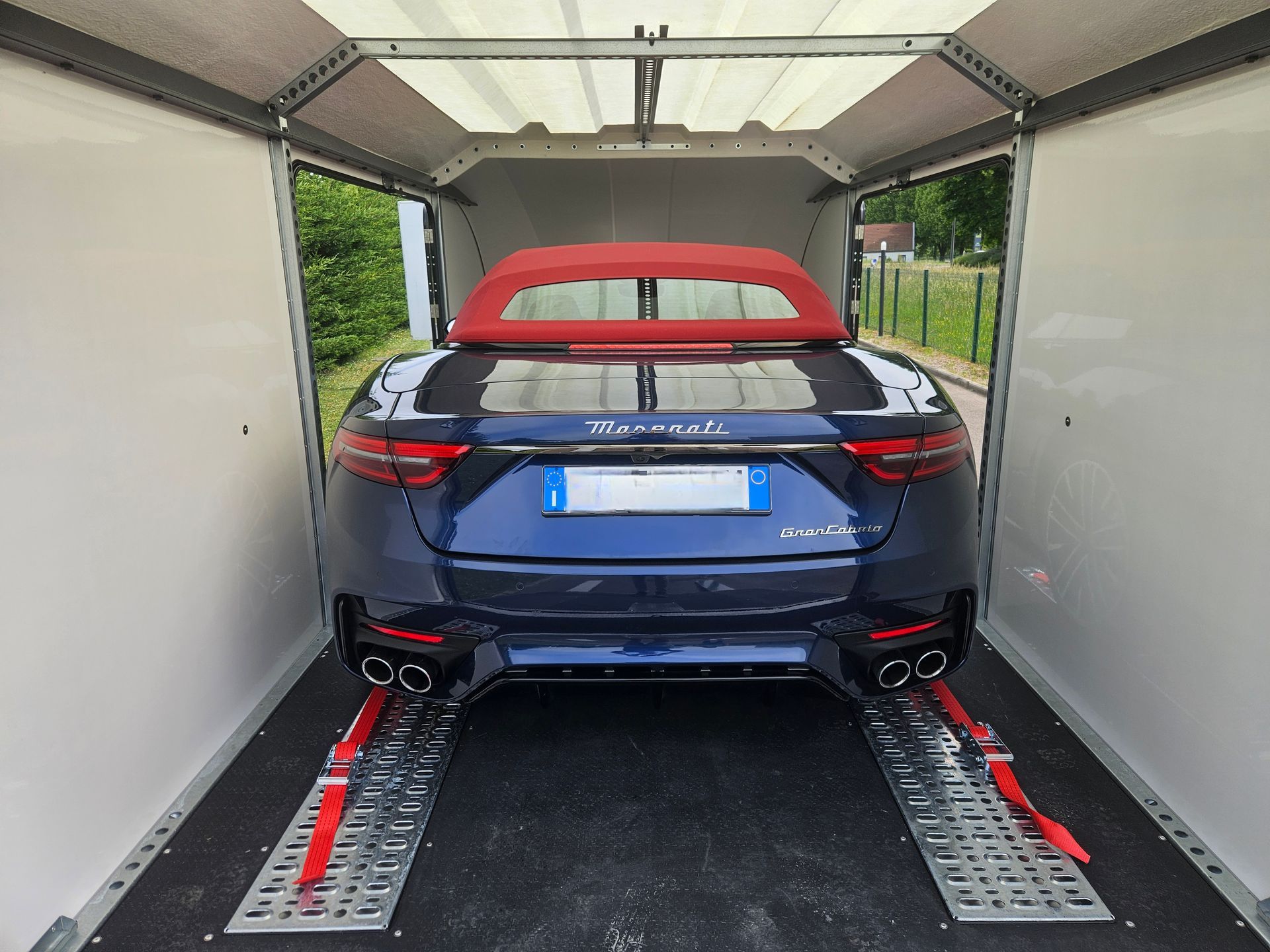 Une Maserati décapotable bleu foncé à capote rouge est arrimée par des sangles rouges à l'intérieur d'une remorque.