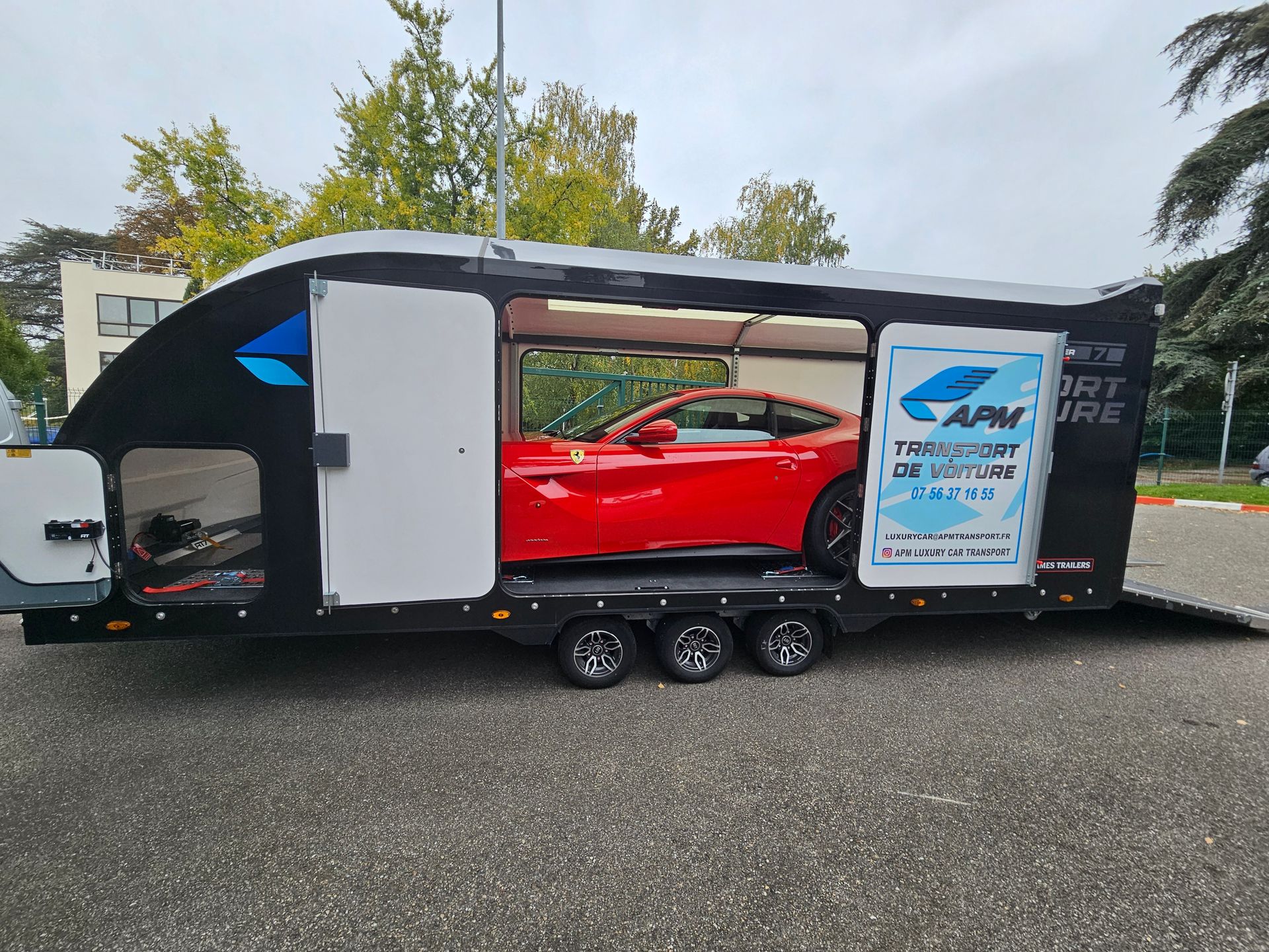 Une Ferrari rouge garée à l'extérieur, dans une remorque porte-voitures noire à trois essieux.