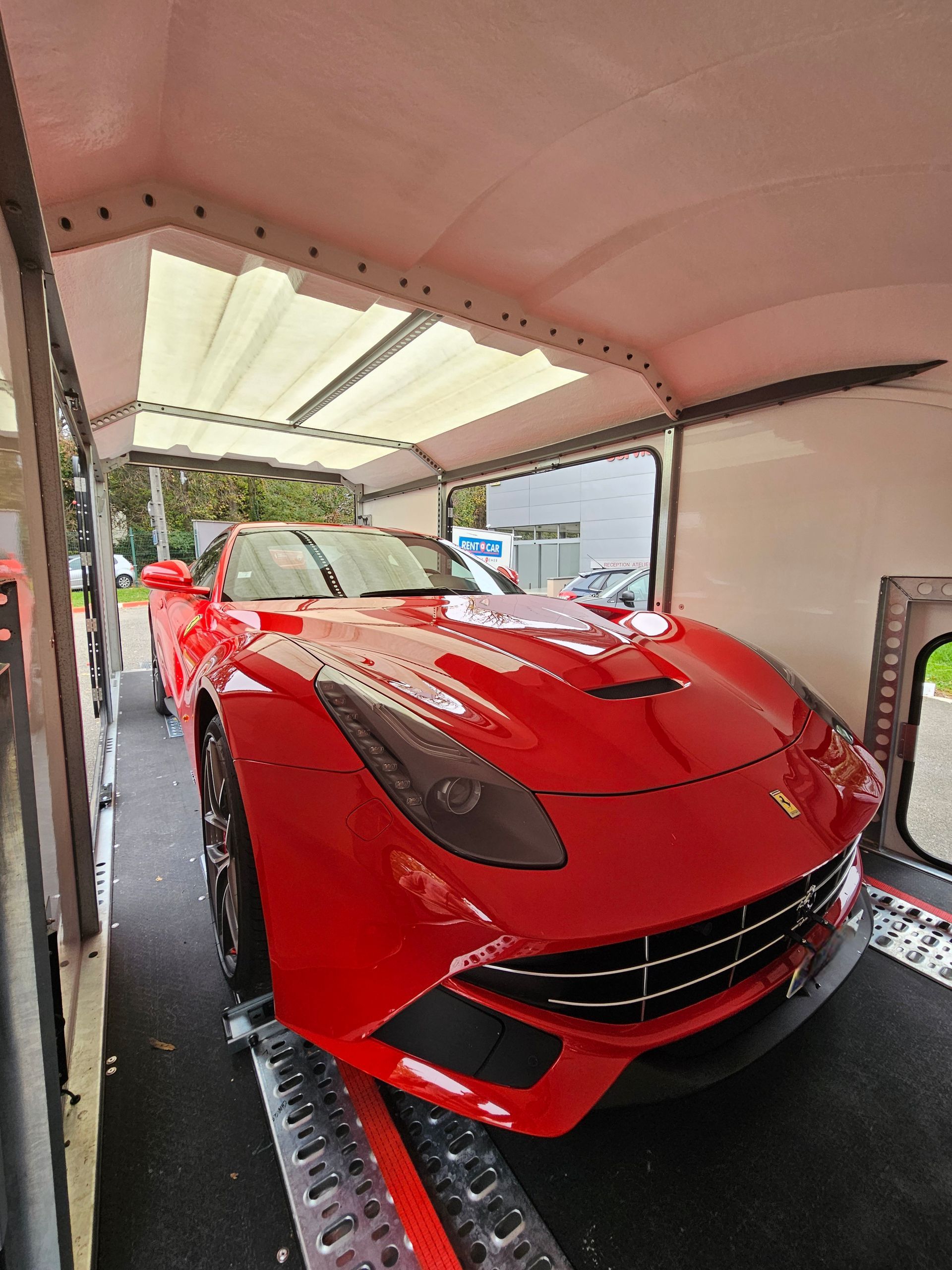 Une Ferrari rouge vif garée à l'intérieur d'une remorque porte-voitures blanche.