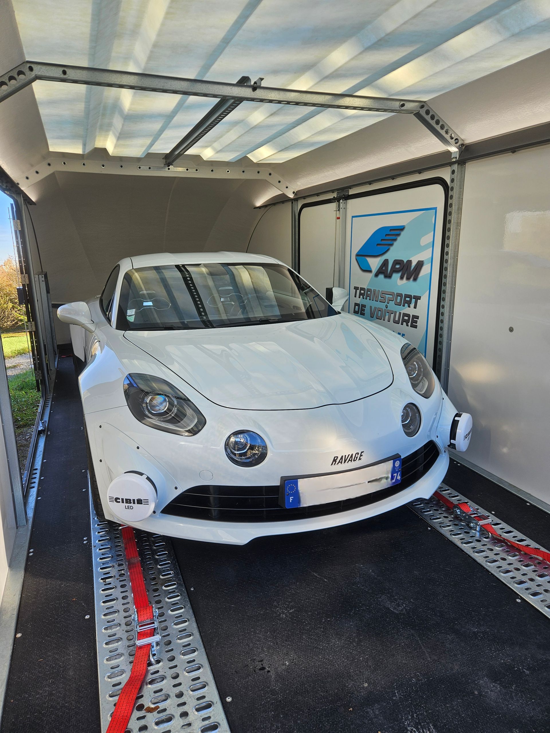 Une voiture de sport Alpine blanche, arrimée par des sangles rouges à l'intérieur d'une remorque de transport.