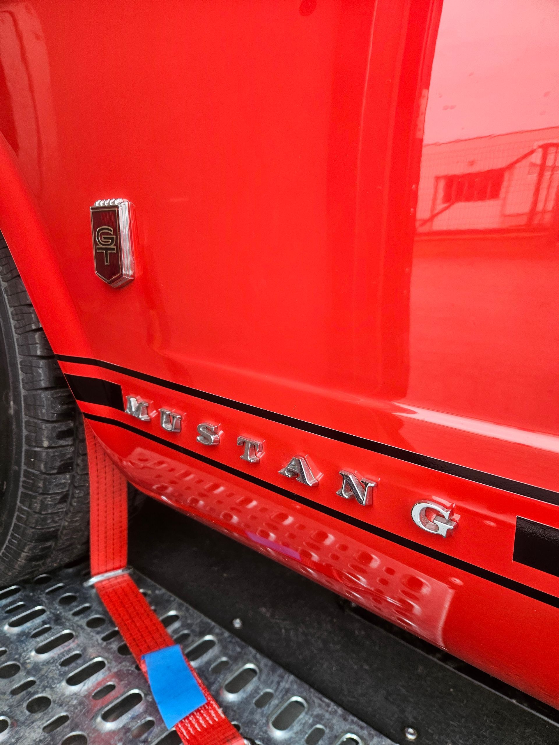 Gros plan sur l'extérieur d'une Mustang rouge vif, avec l'inscription chromée « Mustang » et un badge.
