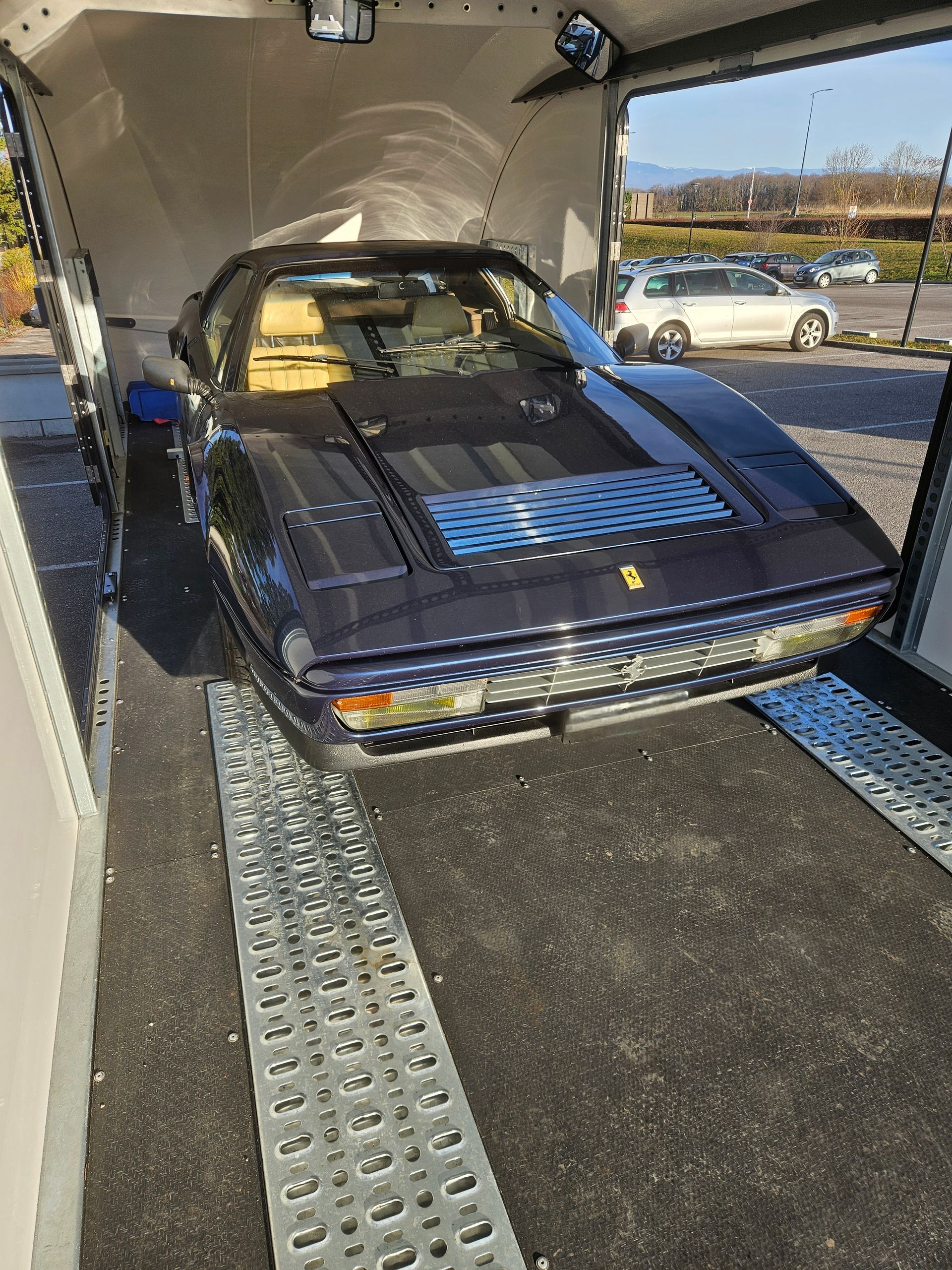 Une Ferrari vintage bleu foncé garée dans une remorque par une journée ensoleillée.
