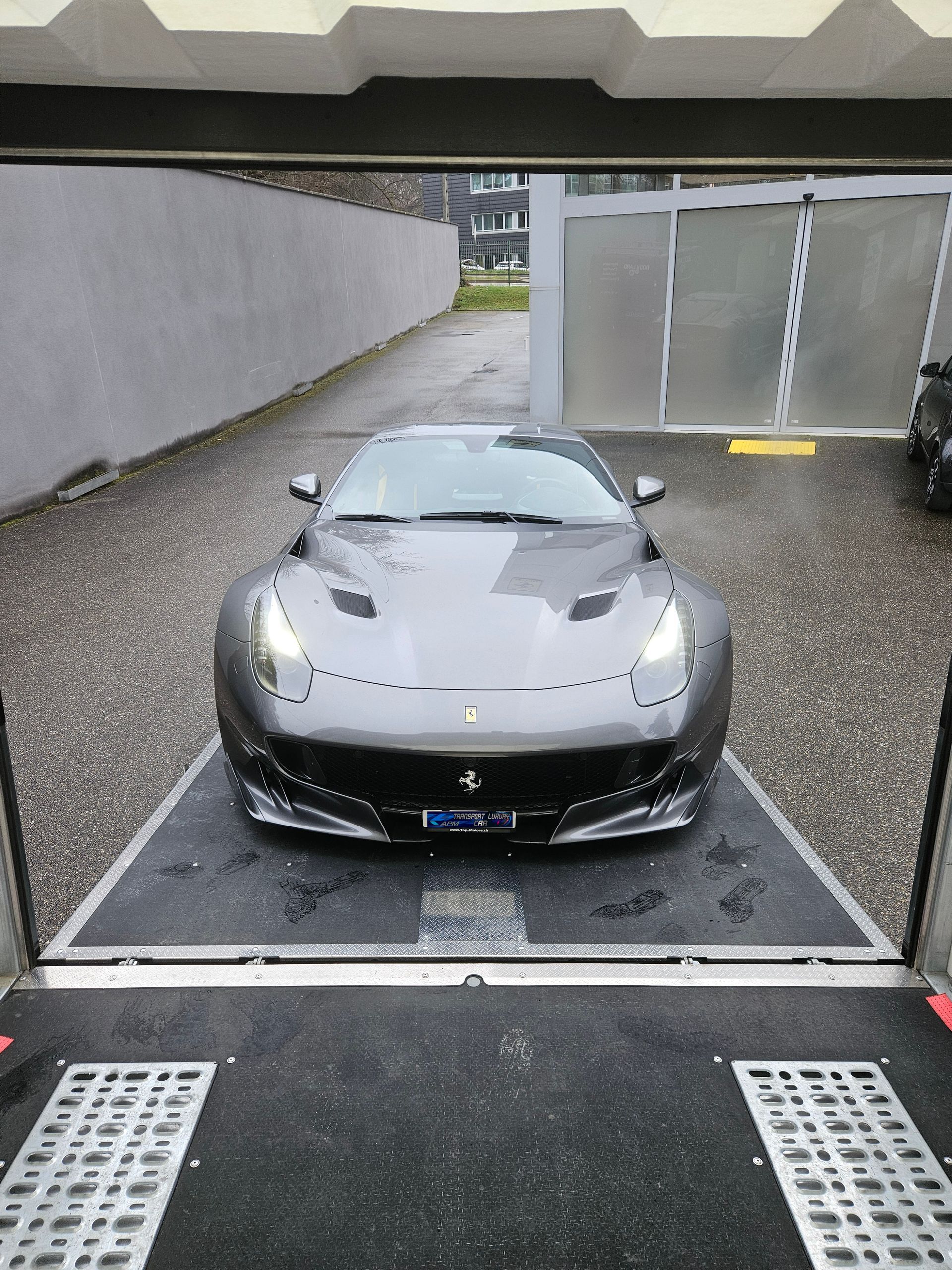 Une Ferrari gris foncé, voiture de sport, est garée sur la rampe de chargement d'une remorque de transport.