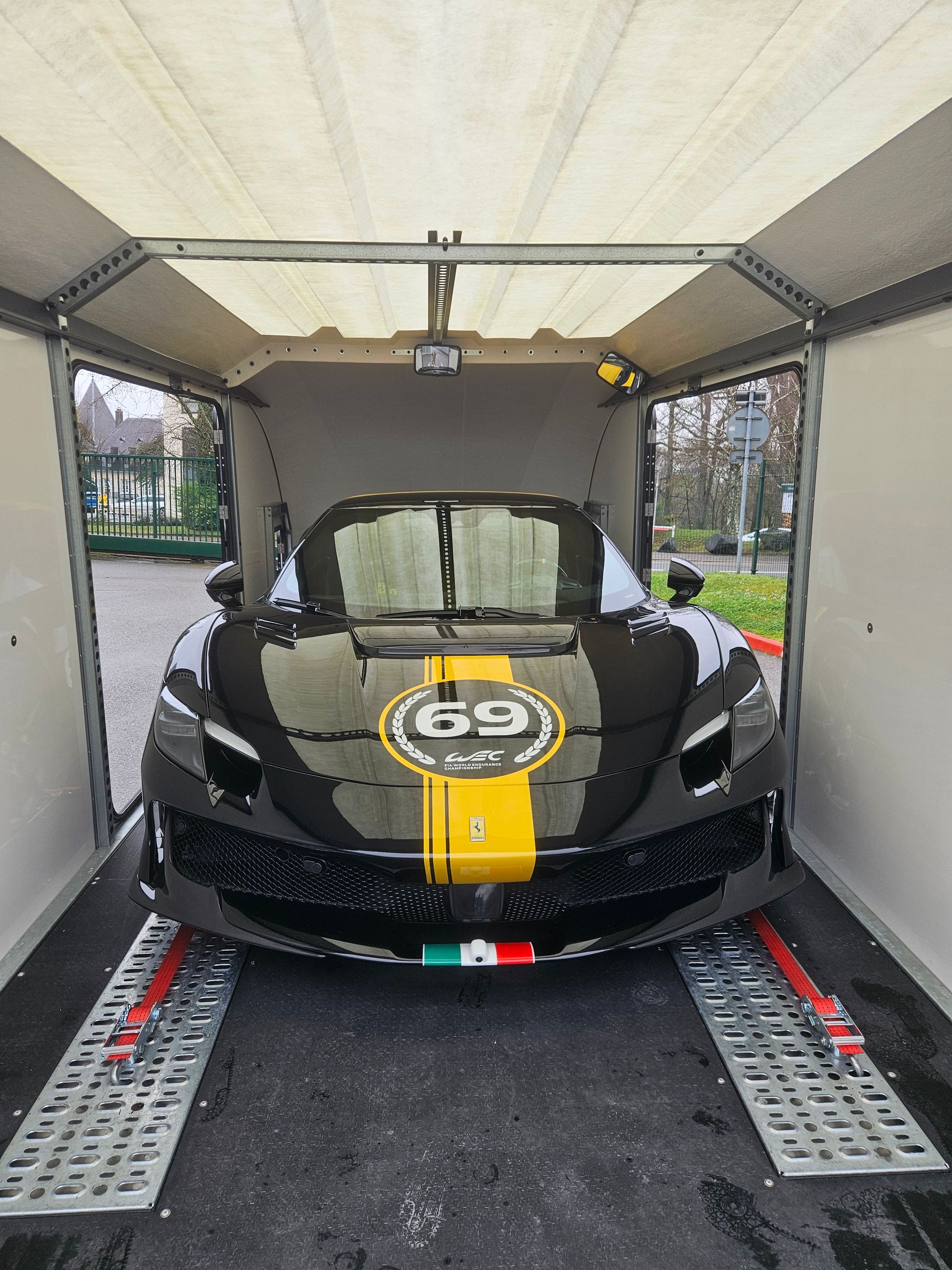 Une Ferrari noire avec une bande de course jaune et le numéro 69 dans un cercle à l'intérieur d'une remorque porte-voitures.