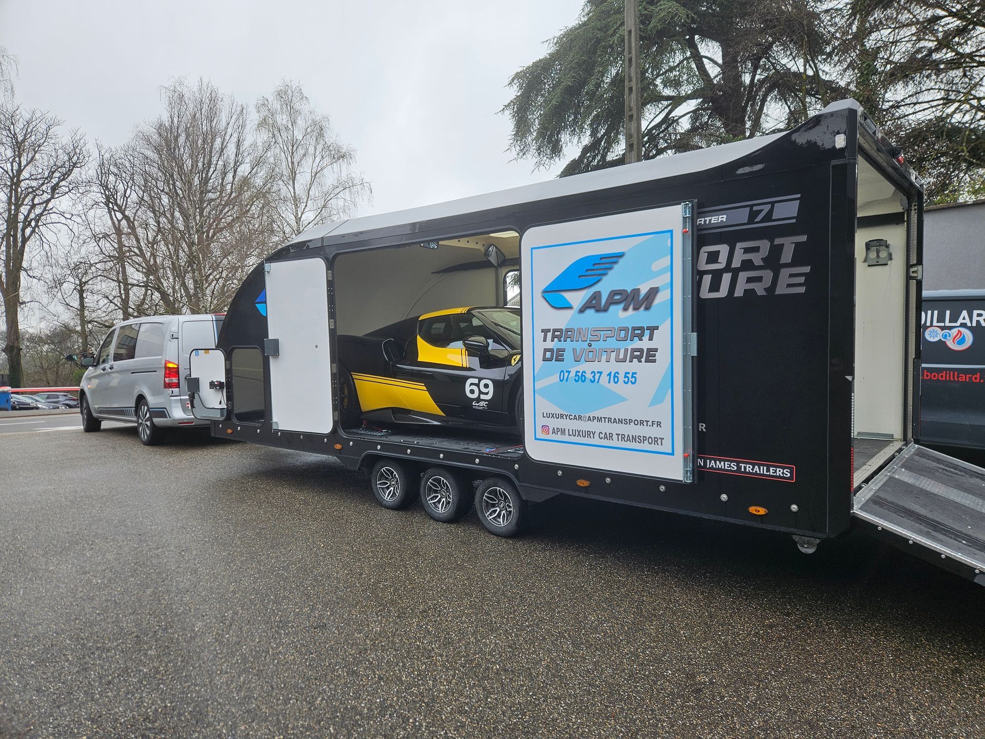 Une remorque noire le côté ouvert, révélant à l'intérieur une voiture de course jaune et noire portant le numéro 69.