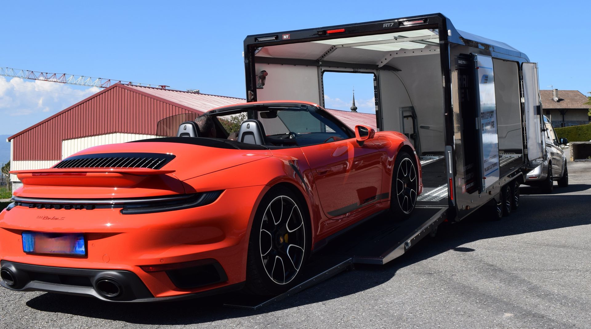 Une Porsche décapotable orange vif est chargée sur une remorque de transport fermée en plein air.