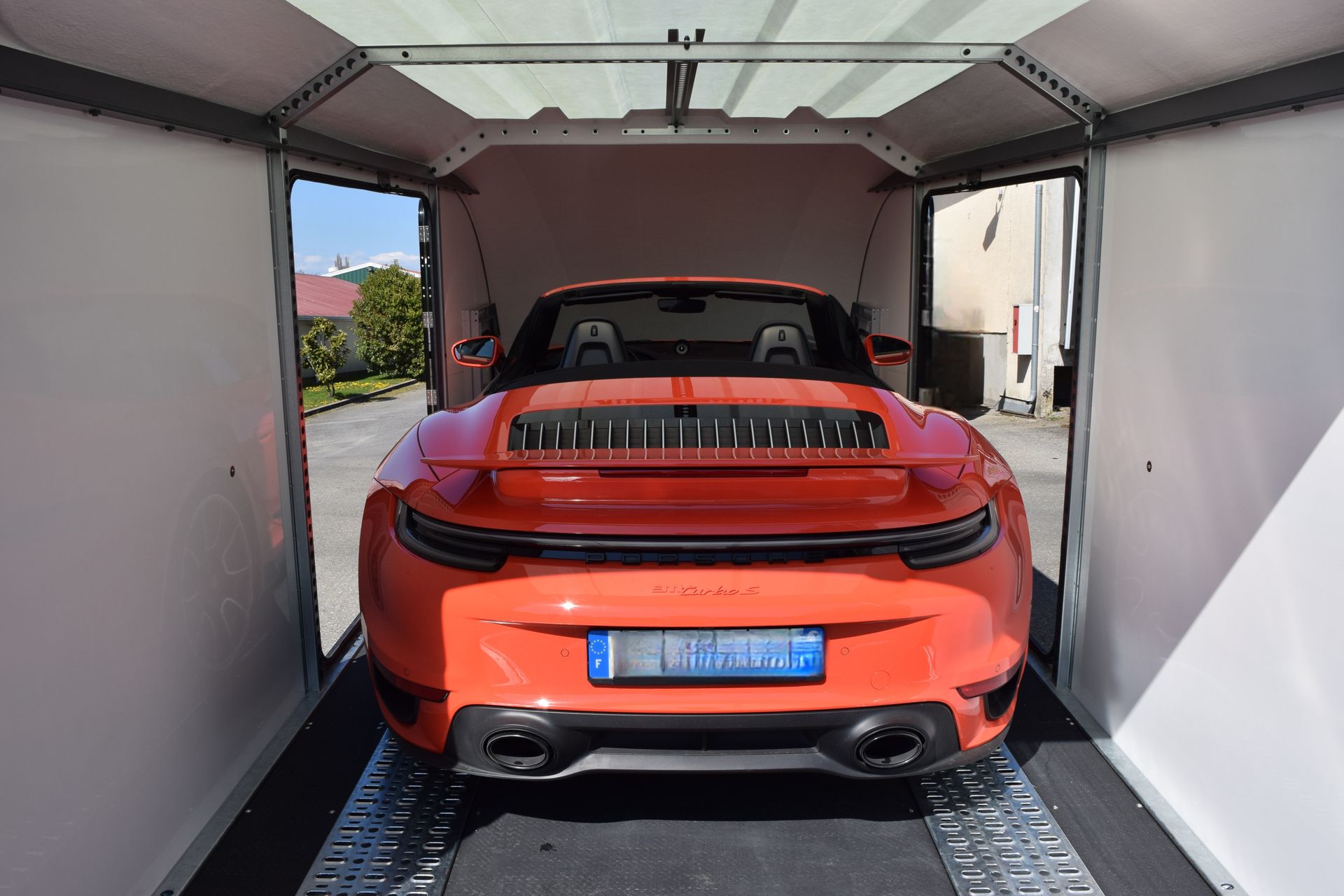 Une Porsche décapotable orange vif garée dans une remorque fermée.