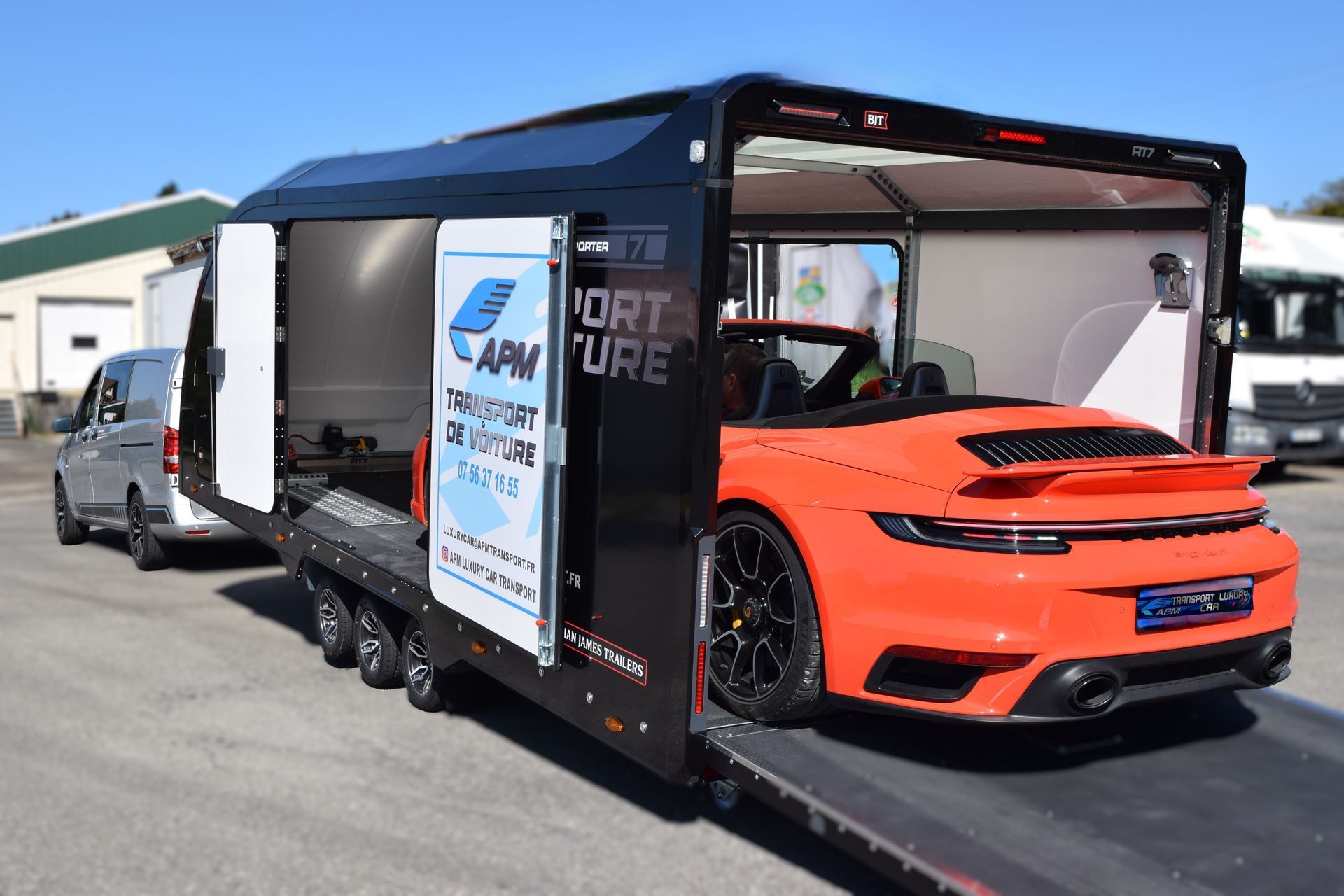 Une Porsche décapotable orange garée à l'intérieur d'une remorque porte-voitures noire ouverte, par une journée ensoleillée.