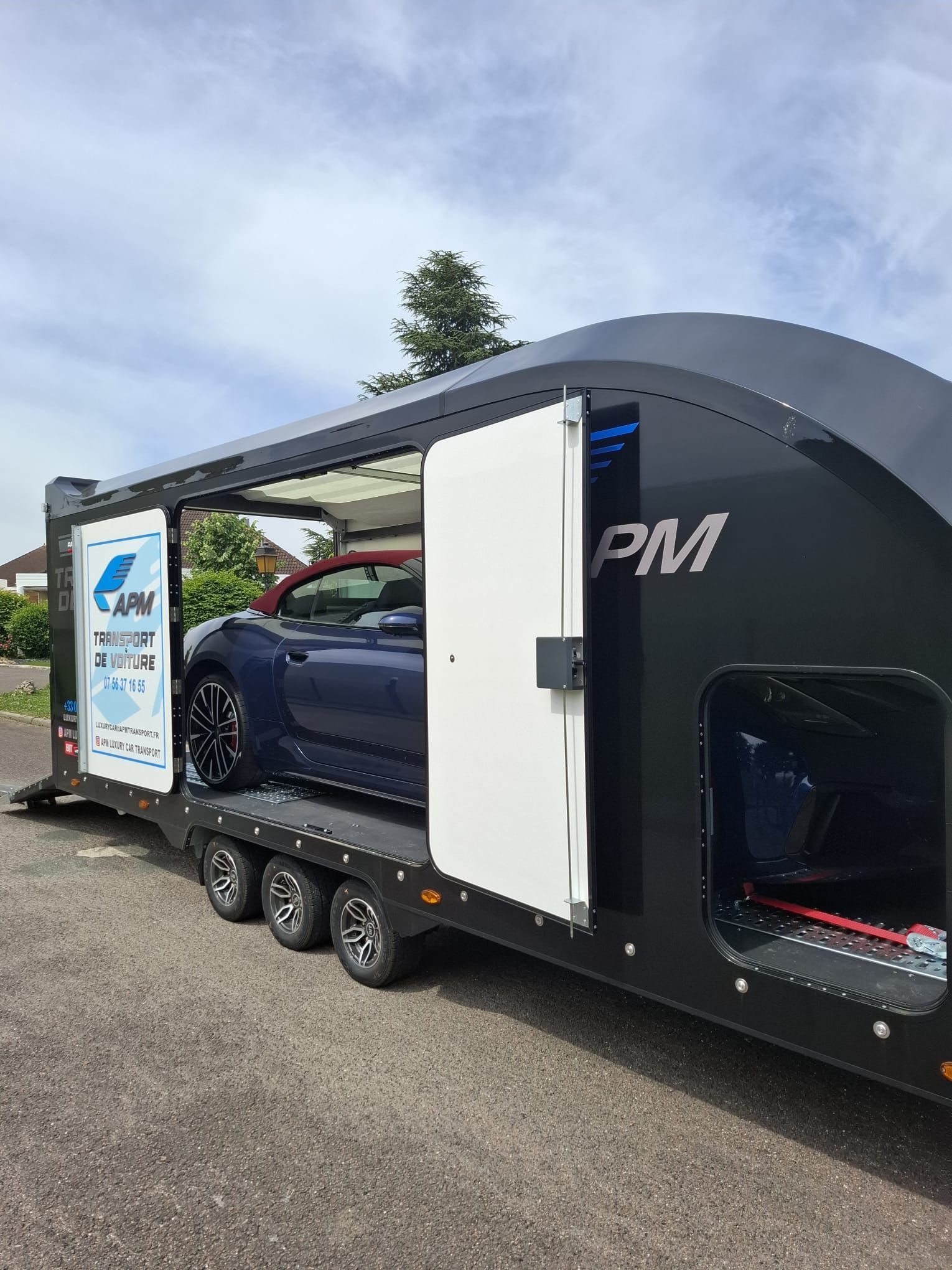 Une voiture de sport bleu foncé chargée dans une remorque noire ouverte et élégante.