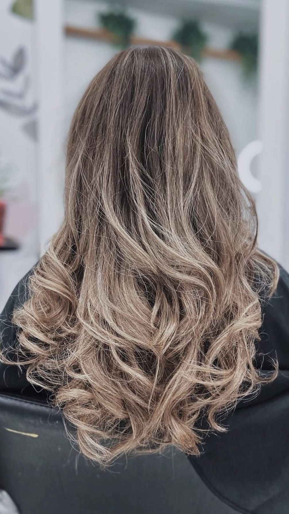 Una mujer con cabello largo y rubio está sentada en una silla en un salón.