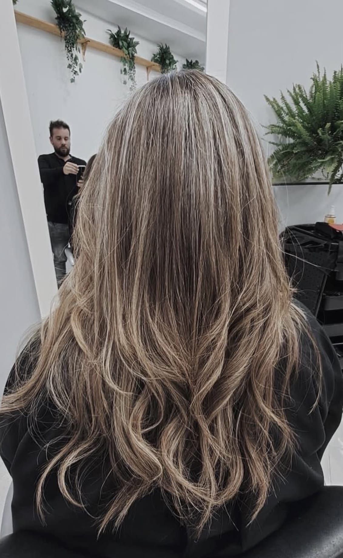 Una mujer con cabello largo y rubio está sentada en una silla en una peluquería.